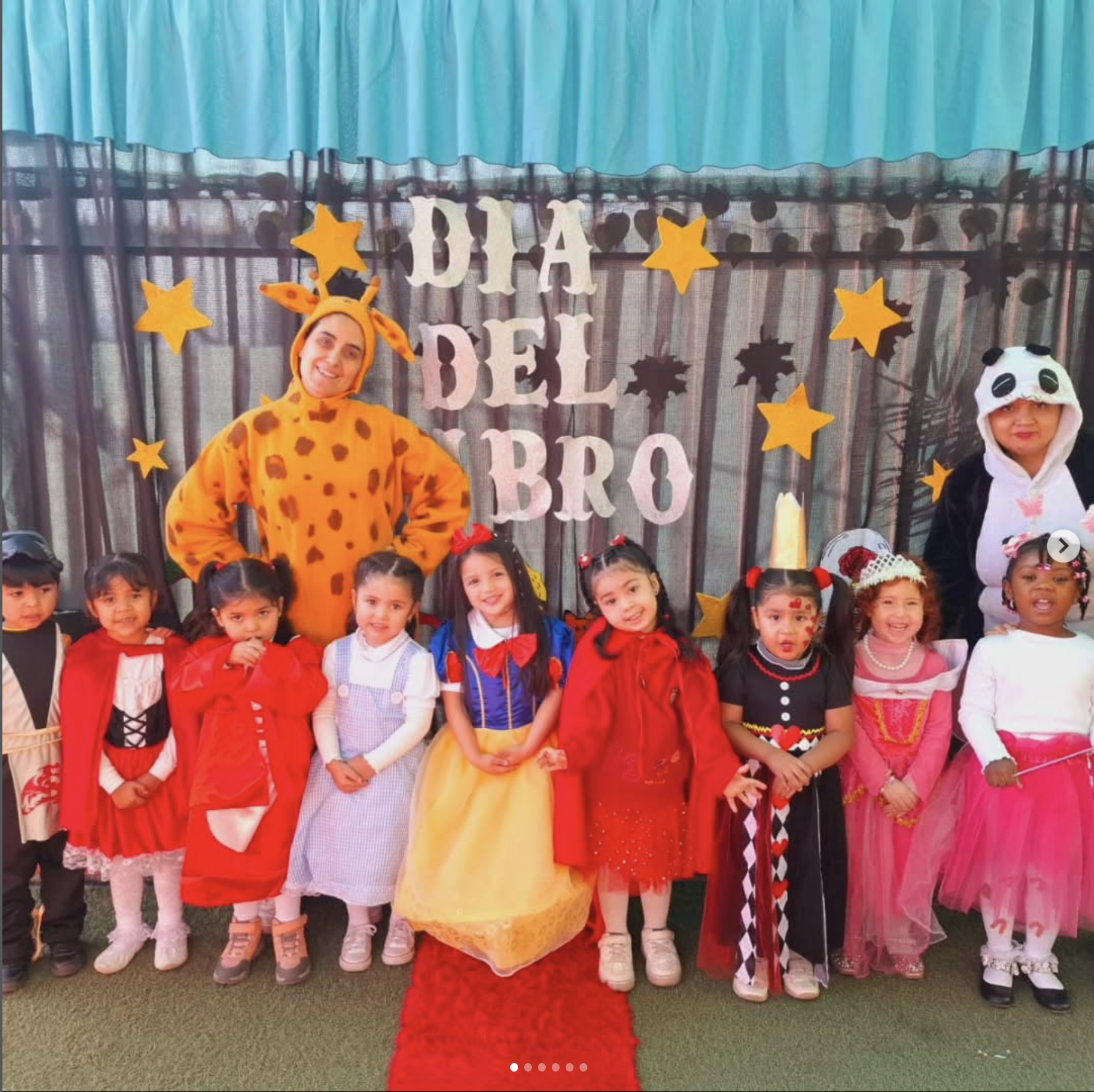 Niños disfrazados de diversos personajes en una celebración del día del niño, con un fondo decorativo y adultos disfrazados de animales