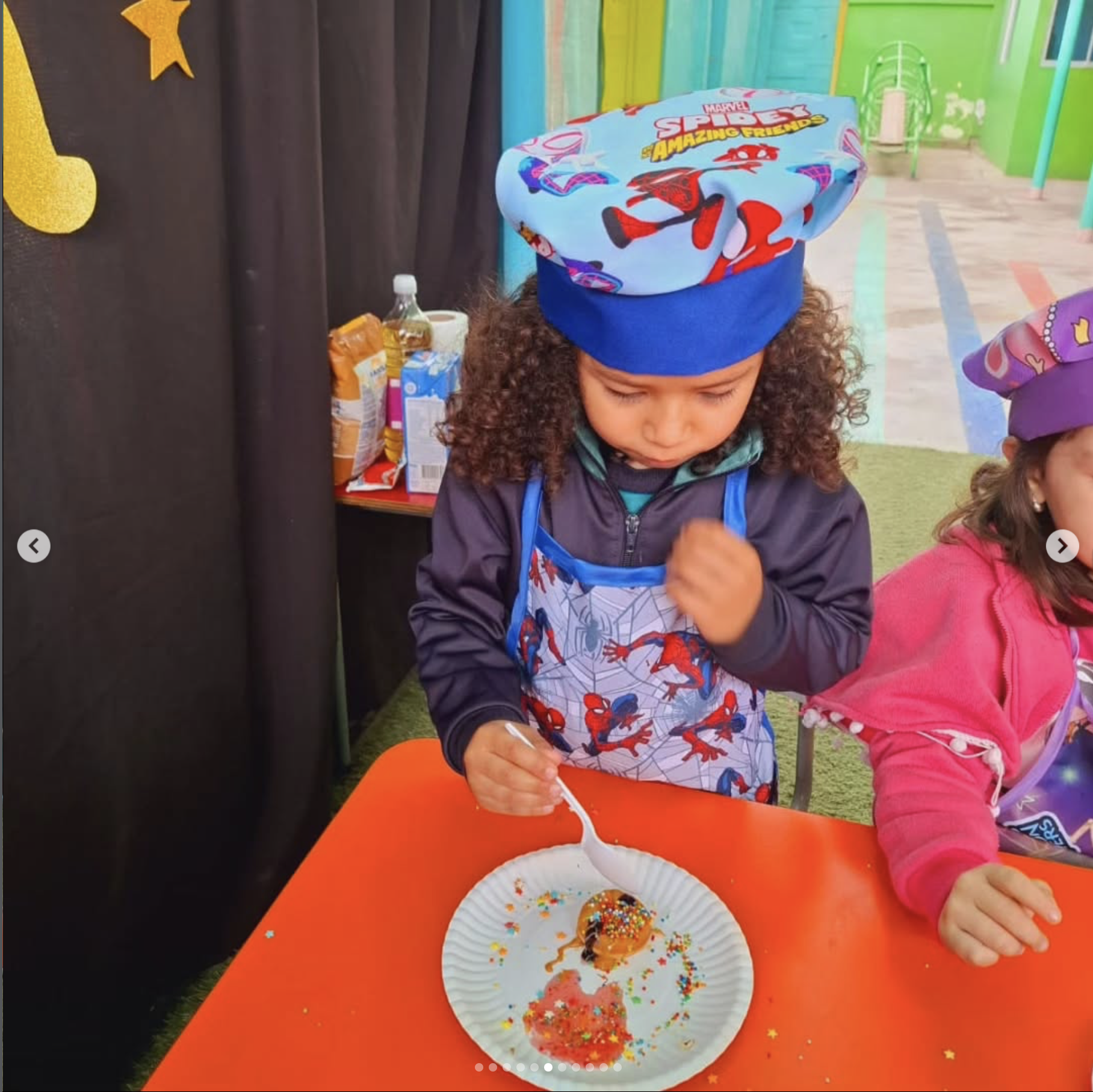 Niña con gorra de Spiderman decorada con personajes de Marvel, participando en una actividad de decorar donas con confites y colorantes, en un espacio colorido y festivo.