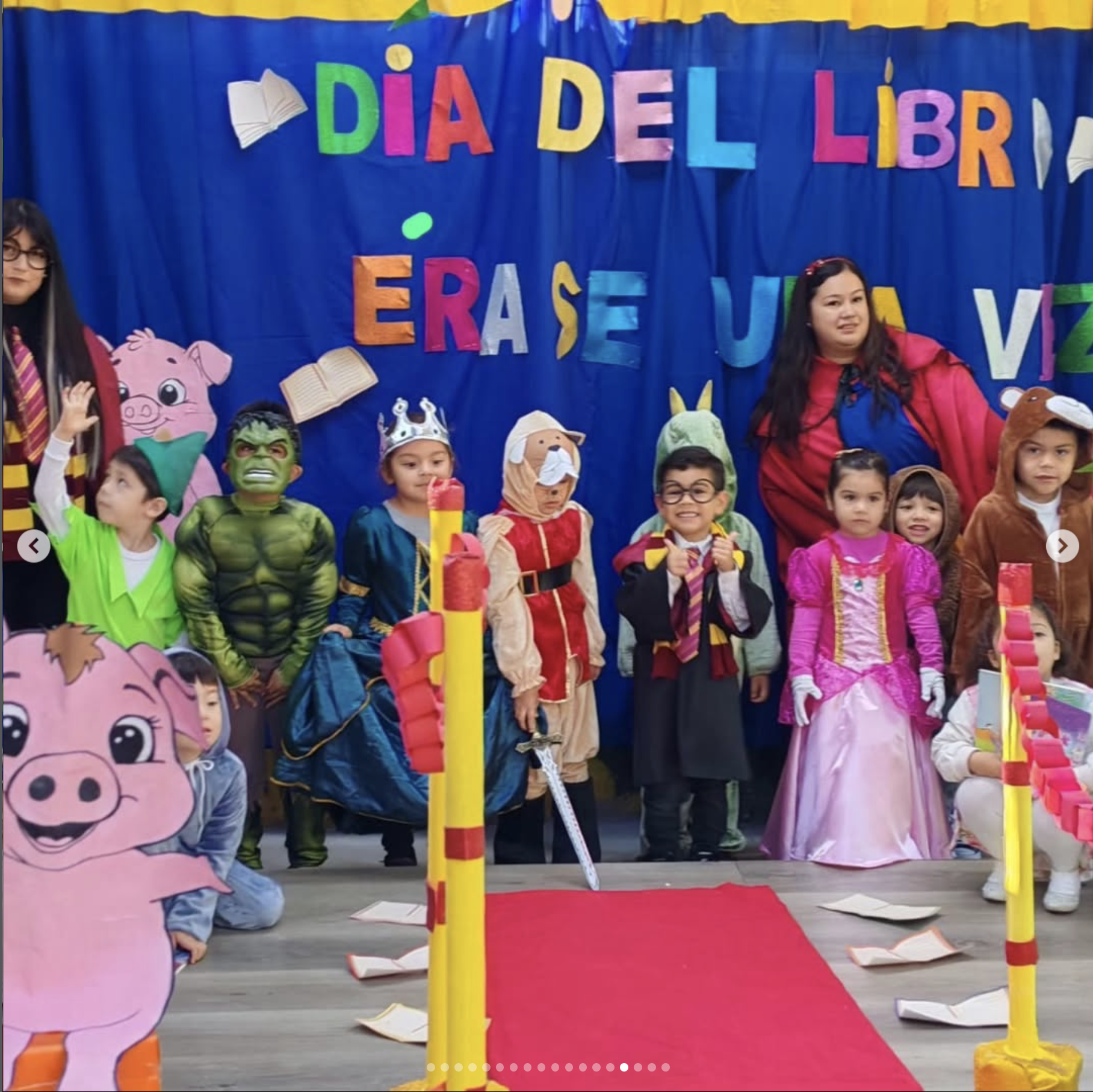 Niños y niñas disfrazados en celebración del Día del Libro en una escuela, con decoraciones de libros y letras coloridas en el fondo.