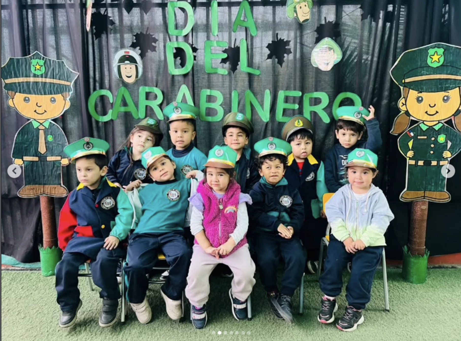 Niños disfrazados de oficiales de policía durante una celebración del Día del Carabinero, con decoraciones de caricaturas y letras verdes en el fondo.