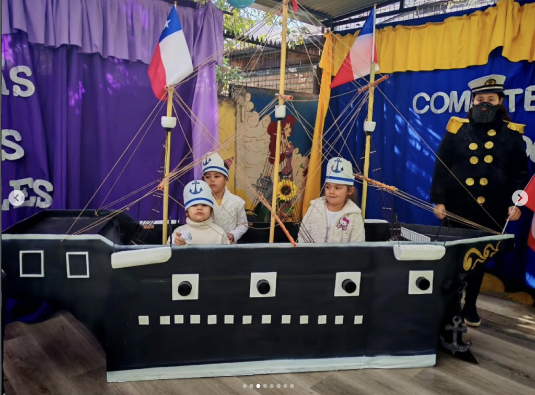 Niños disfrazados de marineros en una actividad escolar, con un decorado de barco y banderas en el fondo.