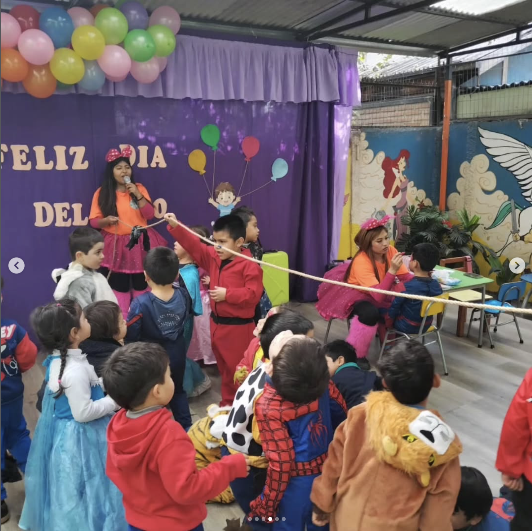 Niños disfrazados en una celebración de Día del Niño, con decoraciones coloridas y globos, en un espacio cerrado con paredes decoradas y figuras de personajes infantiles.