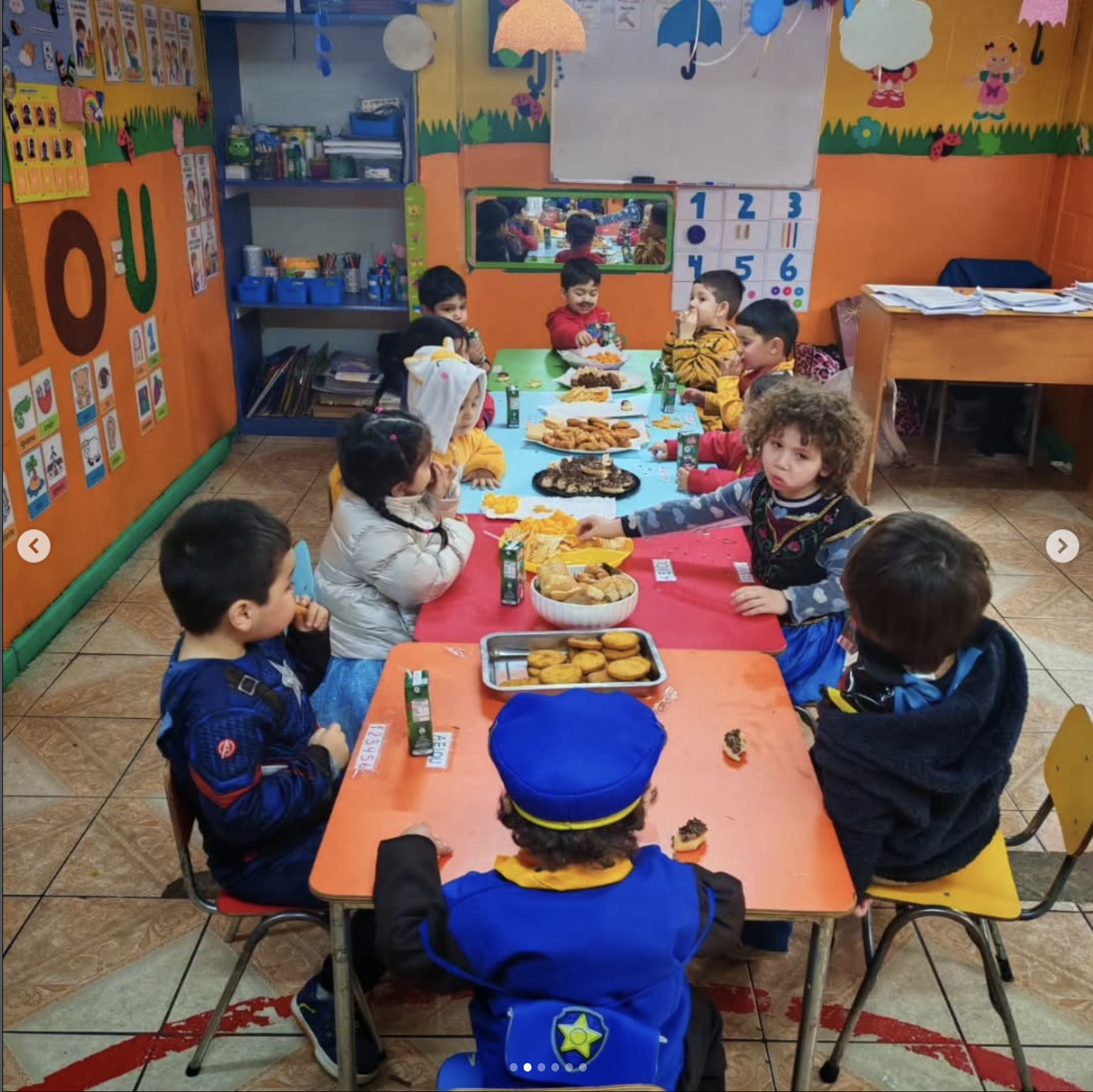 Niños en una fiesta de cumpleaños en un salón decorado con temas infantiles, sentados alrededor de una mesa con comida y bebidas, algunos niños con disfraces.