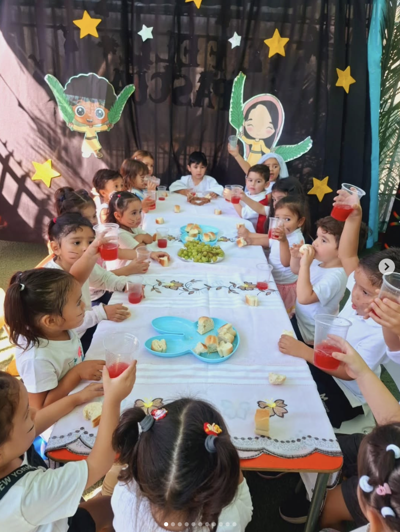 Niños en una fiesta infantil vestidas con ropa blanca y decoraciones con temática de estrellas y personajes infantiles, celebrando alrededor de una mesa con comida y bebidas.