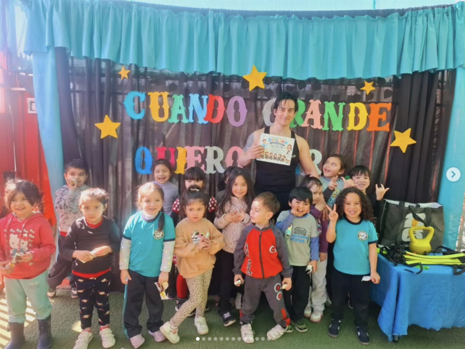 Un grupo de niños y una mujer sosteniendo un diploma en una celebración infantil. Detrás, un cartel decorativo con letras coloridas que dice 'Cuando grande quiero ser'.