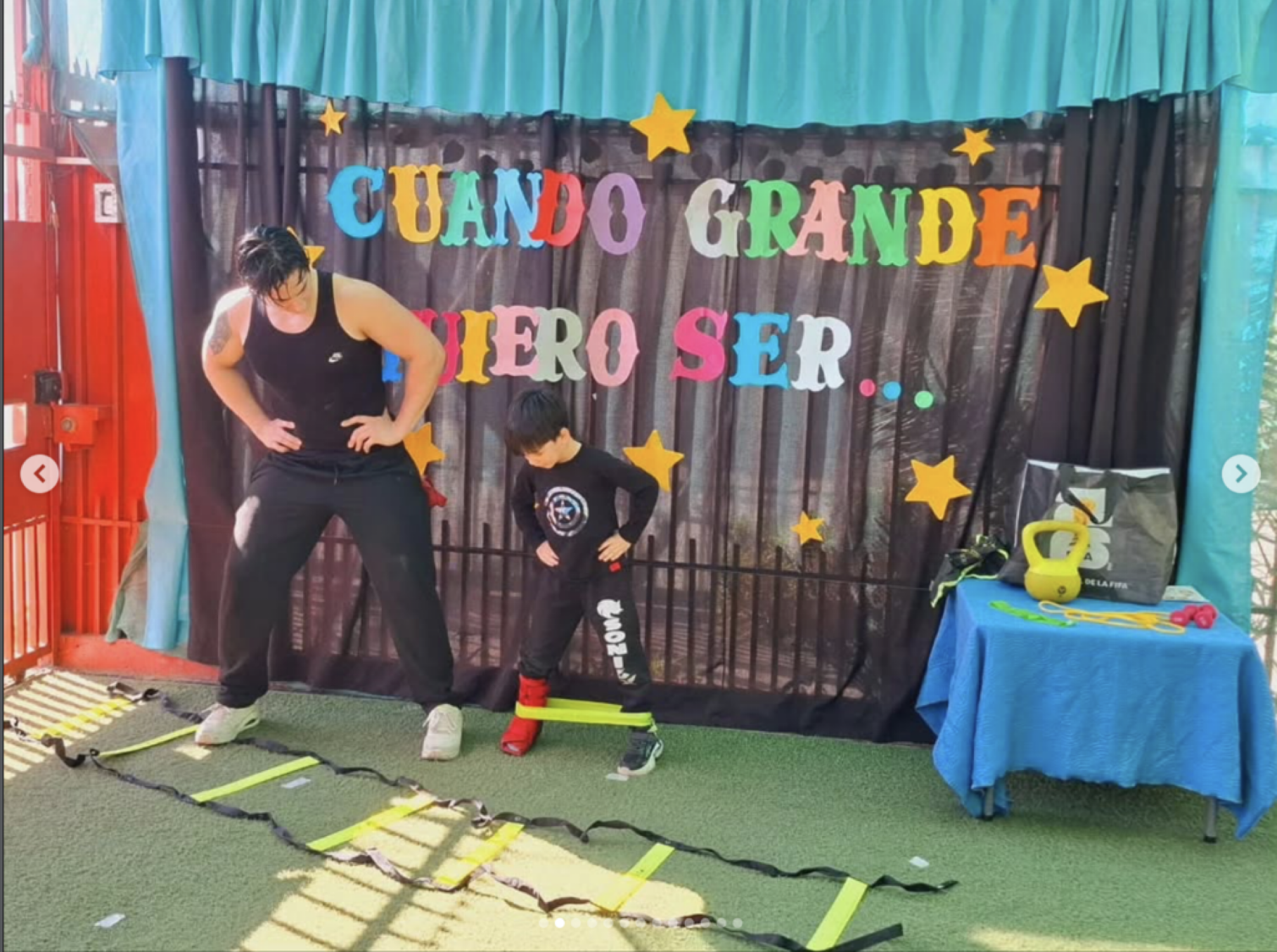 Escenario con decoración colorida, niños y un adulto participan en una actividad física con escaleras y cuerdas de agilidad en un espacio cubierto con cortinas azules. En el fondo cartel con letras de colores y estrellas que dice 'CUANDO GRANDE QUIER