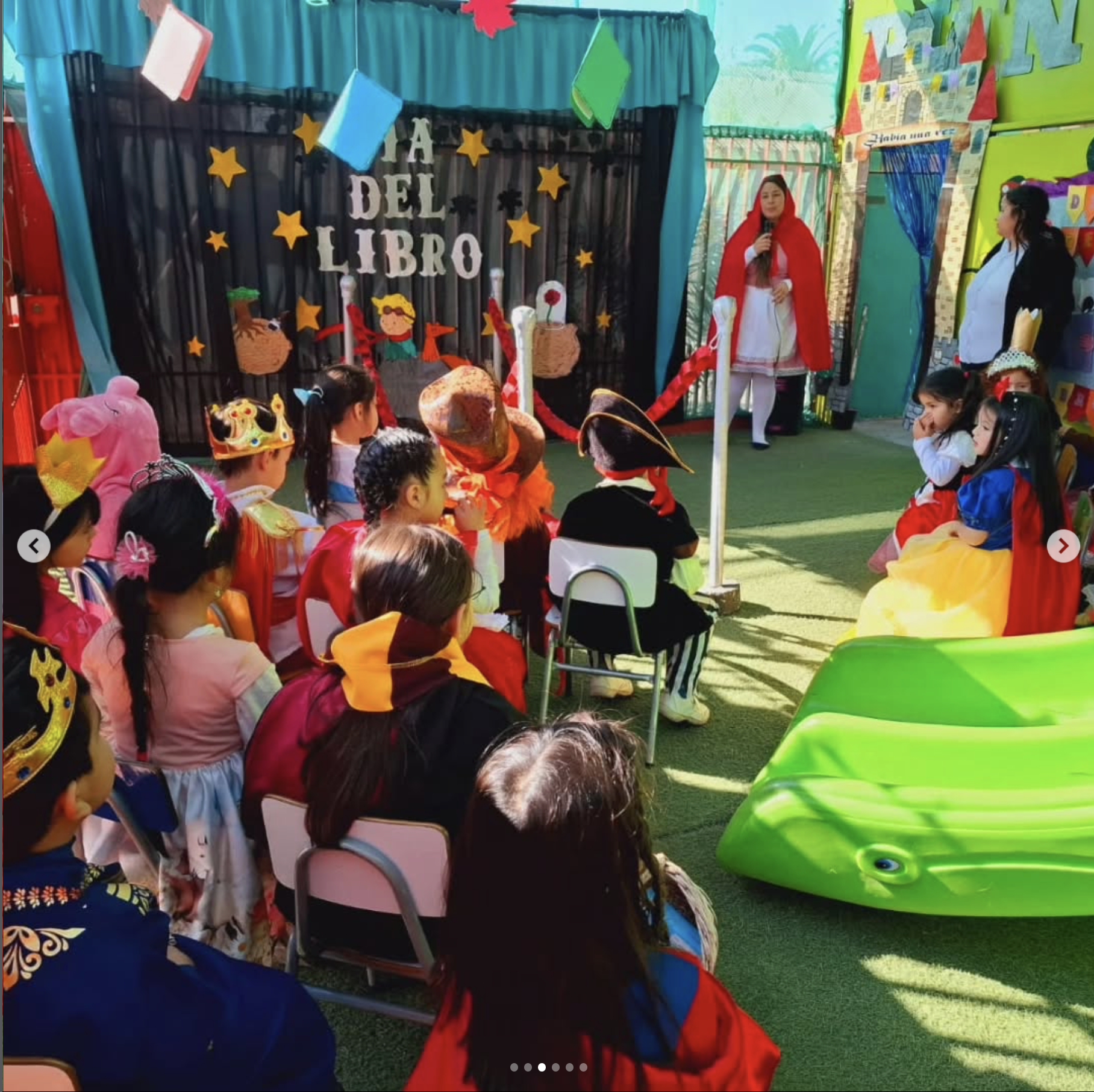 Niños disfrazados en un evento temático infantil con decoración de libros y castillos, participando en una actividad escolar, con una niña vestida de Caperucita Roja hablando frente a la audiencia.