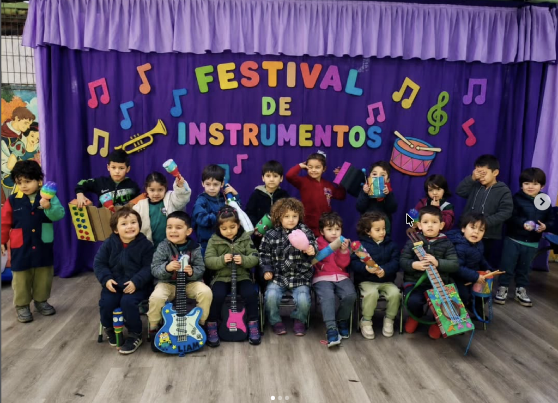 Grupo de niños en un escenario escolar con decoraciones musicales, sosteniendo instrumentos musicales y objetos artesanales