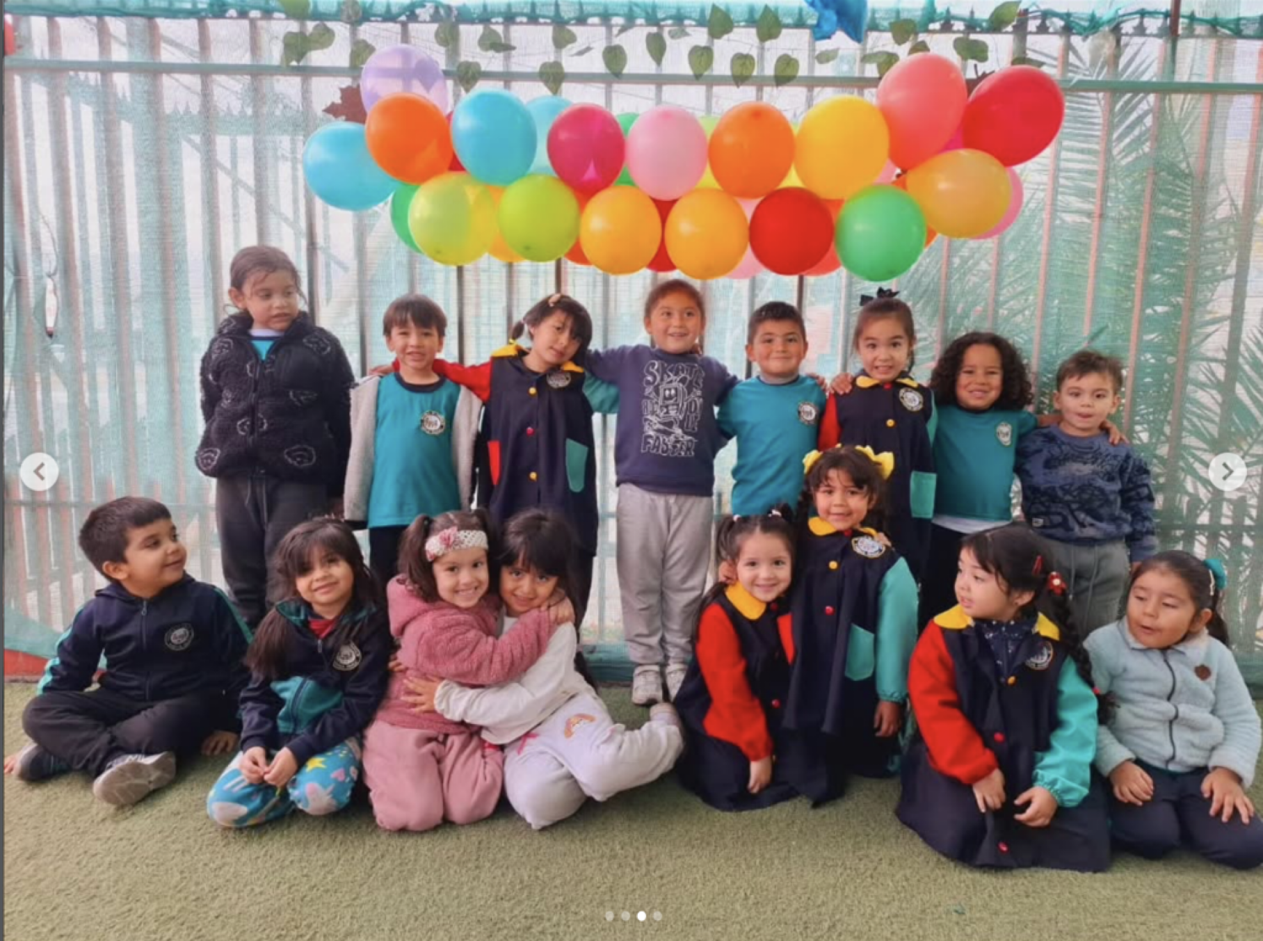 Grupo de niños y niñas de primaria en una celebración, con globos de colores en el fondo y algunos niños en la parte frontal posando para la foto.