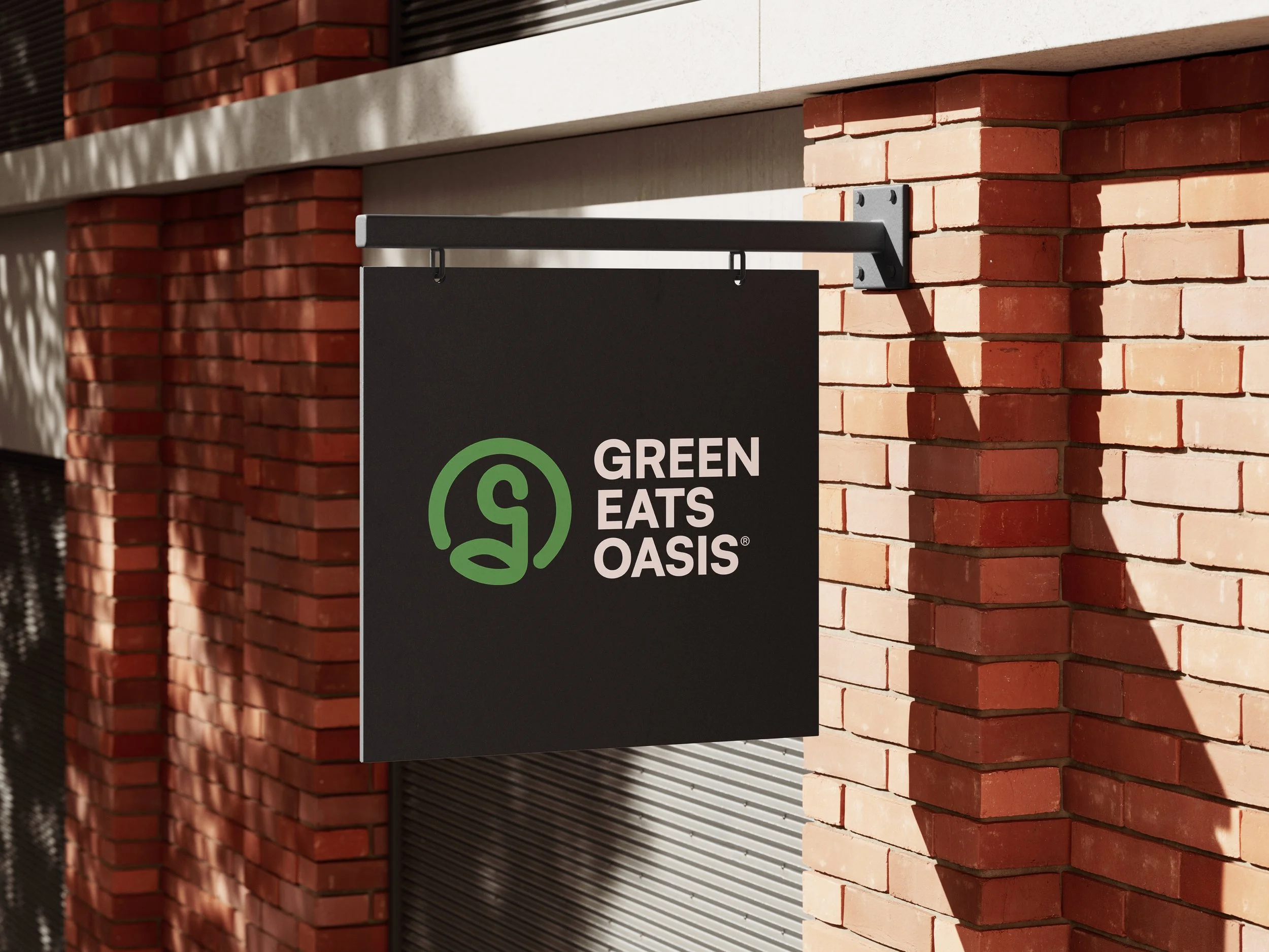 Close-up of a brick wall with a black sign that reads 'GREEN EATS OASIS' hanging from a metal bracket.