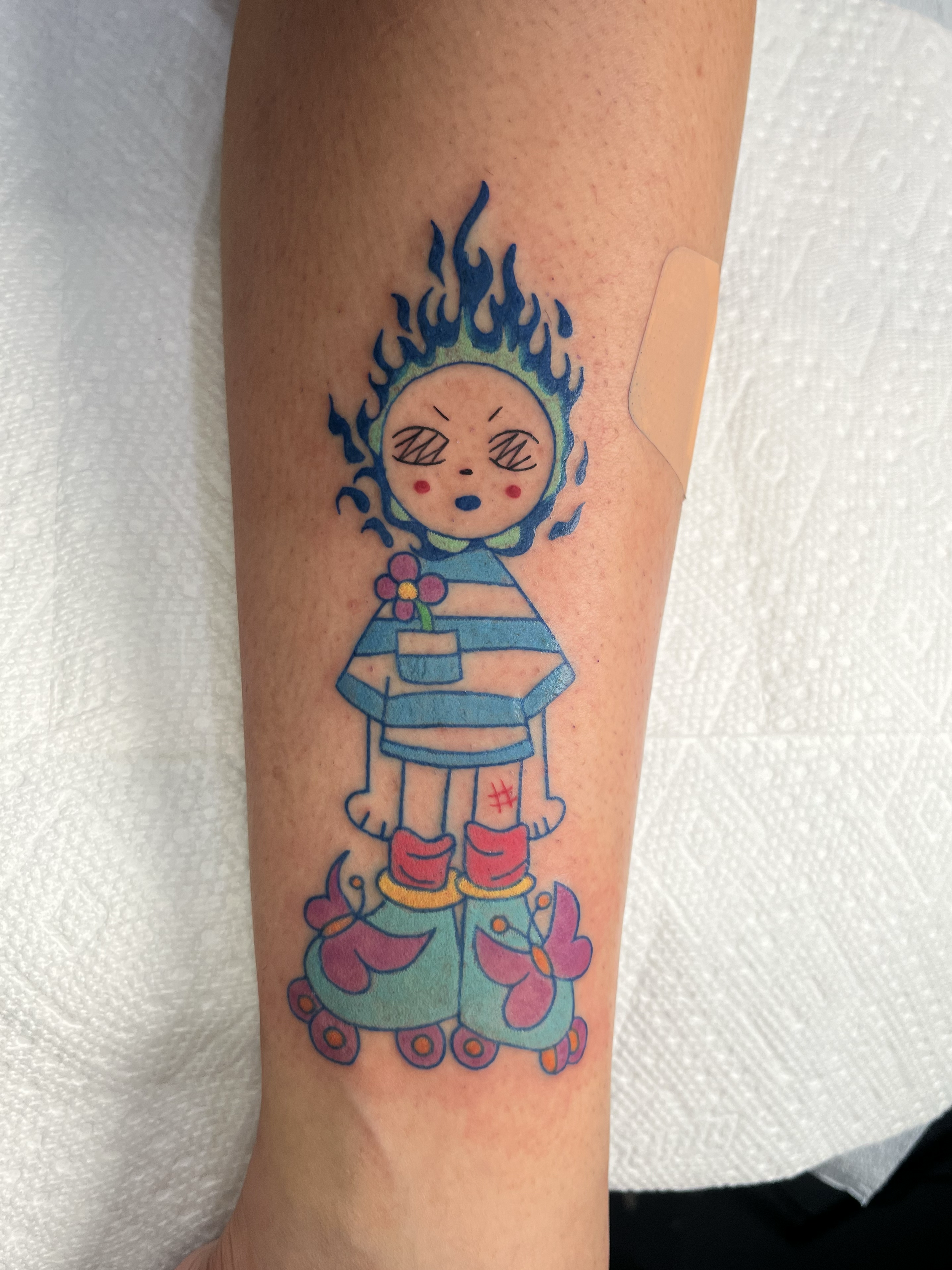 Colorful tattoo of a girl with a flame-like hairdo, holding a flower, standing on a skateboard, on a person's arm.