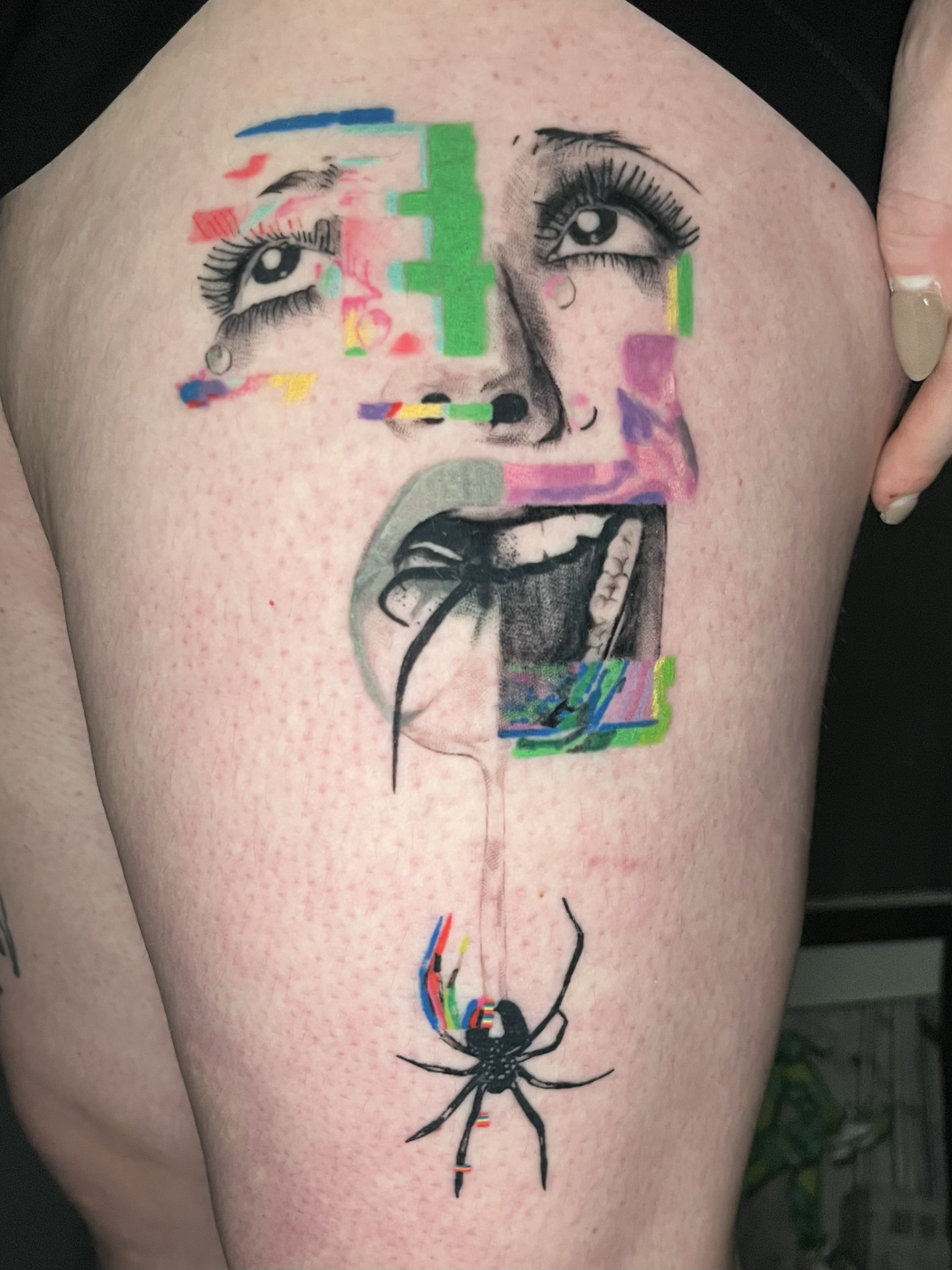 A tattoo of a woman's face, with expressive eyes and open mouth, overlaid with digital glitch effects in vibrant colors, and a black spider hanging below.
