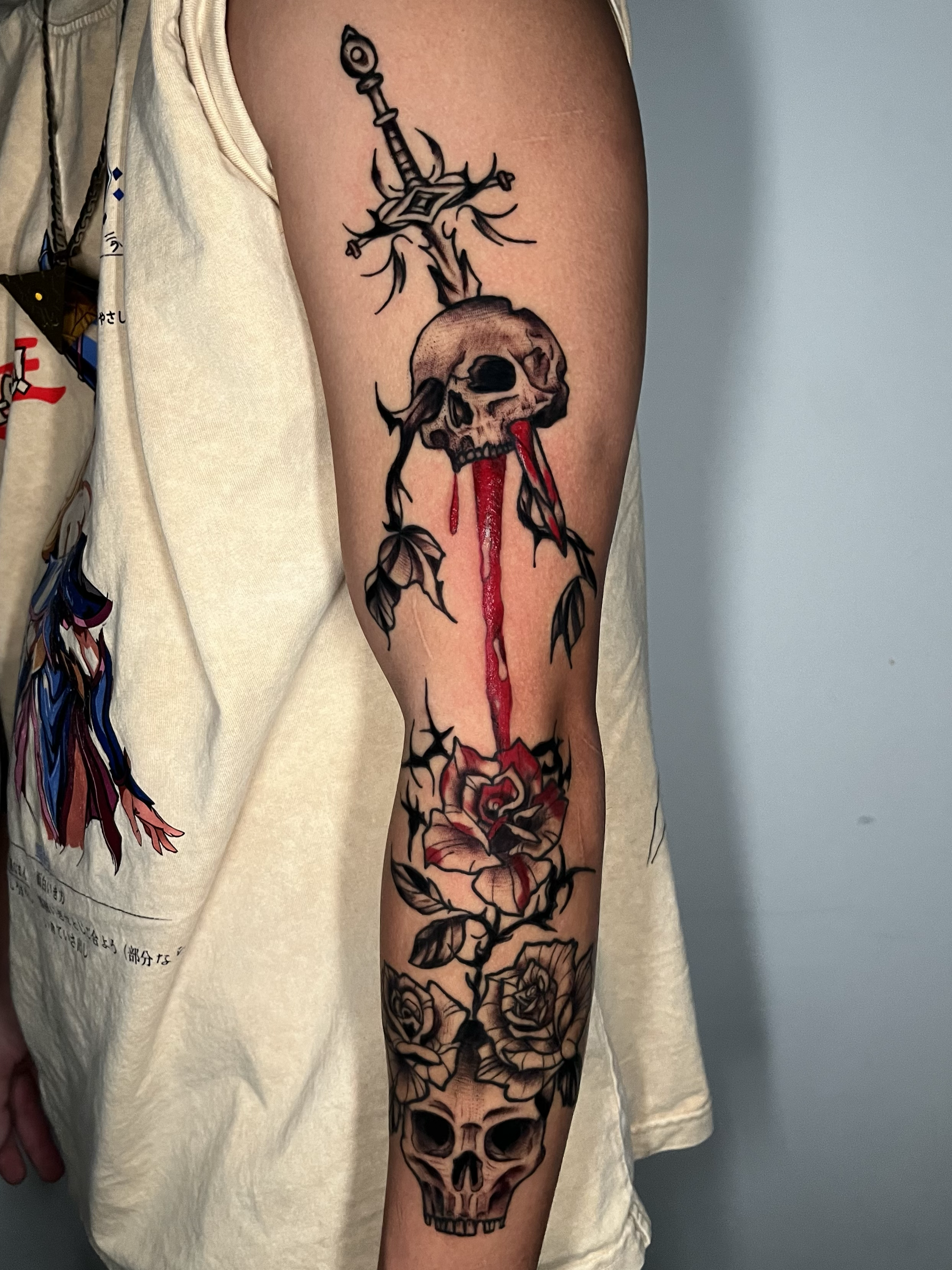 Tattoo of a skull with roses, a dagger, and black ink accents on a person's arm.