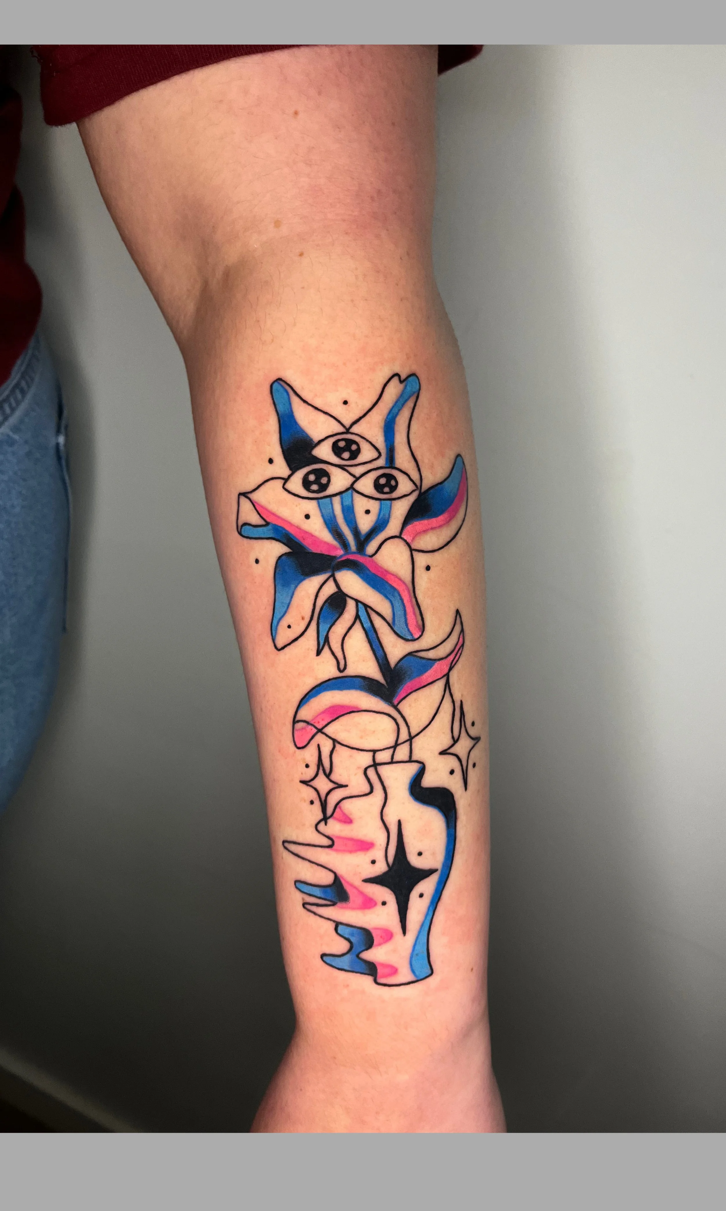 Tattoo of a colorful abstract floral design with eyes and stars on a person's forearm.