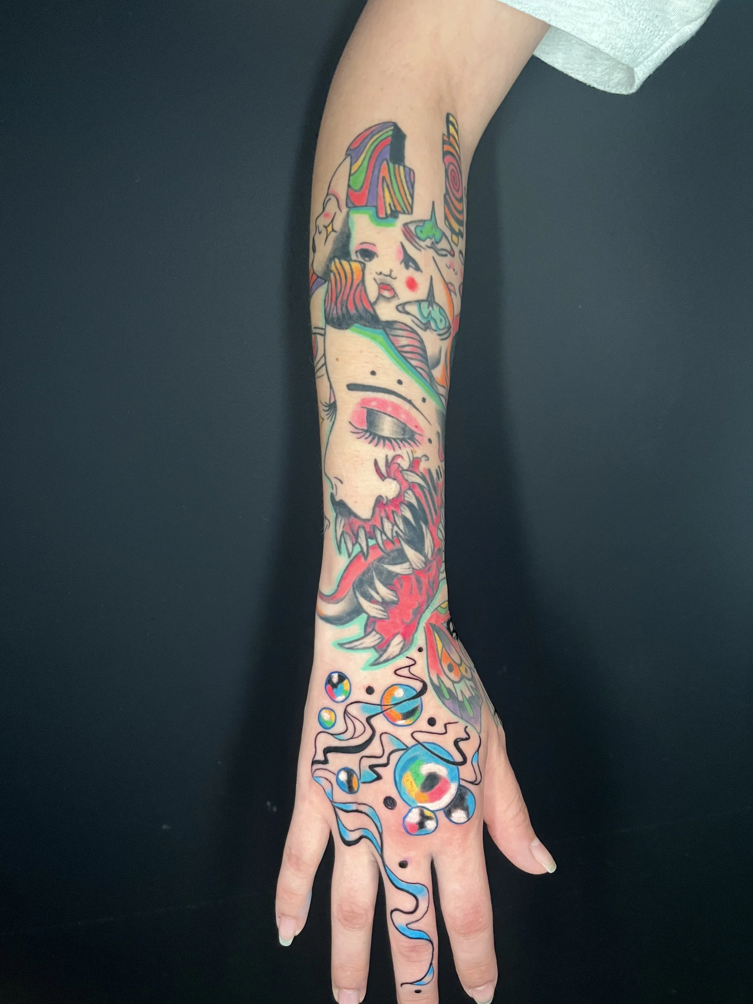Tattooed hand with colorful, abstract, and surreal artwork including a face, a unicorn, planets, and various geometric shapes.