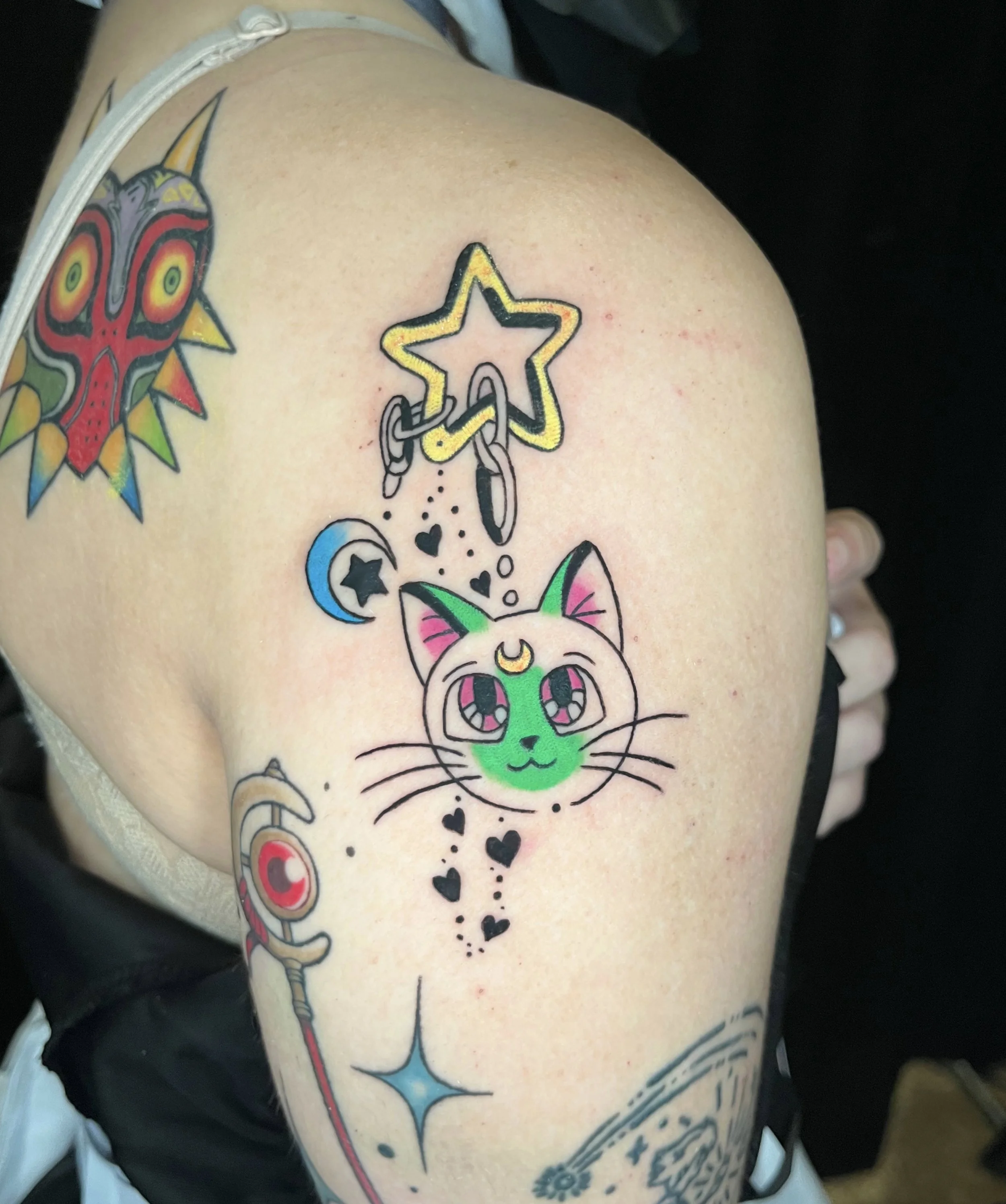 Tattooed shoulder featuring colorful, cartoon-style designs of a star and a cat's face with neon green accents.