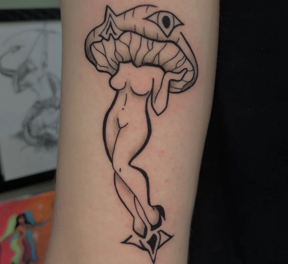 Tattoo of a woman with a mushroom cap as the head, with a sword-like shape at the bottom, black outlines, on skin.