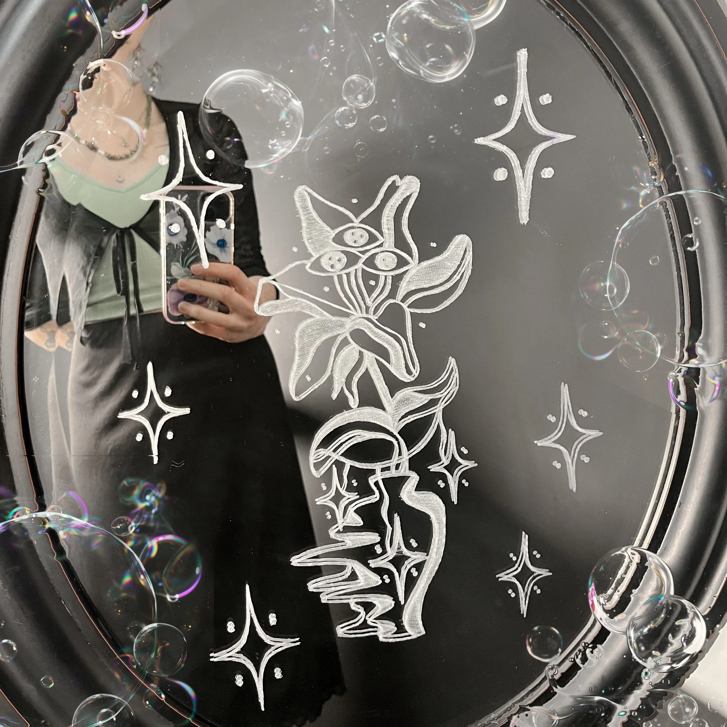 A mirror with a white chalk or paint drawing of a flower, bubbles, and other decorative elements on its surface.