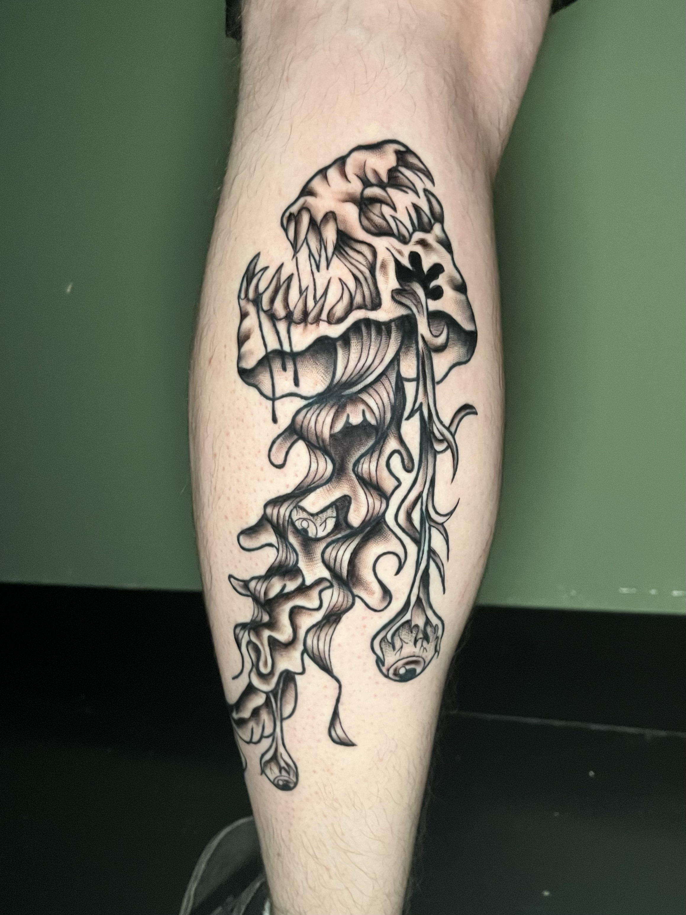 A detailed black and gray tattoo of a screaming wolf with flowing lines extending down the person's leg.