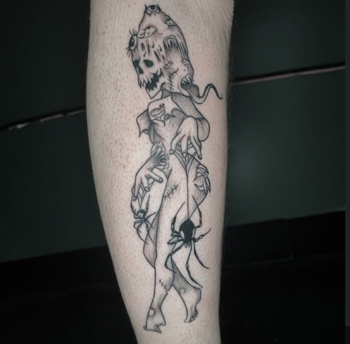 Tattoo of a skeleton with a skull head, holding out an insect, with a spider hanging from its leg.