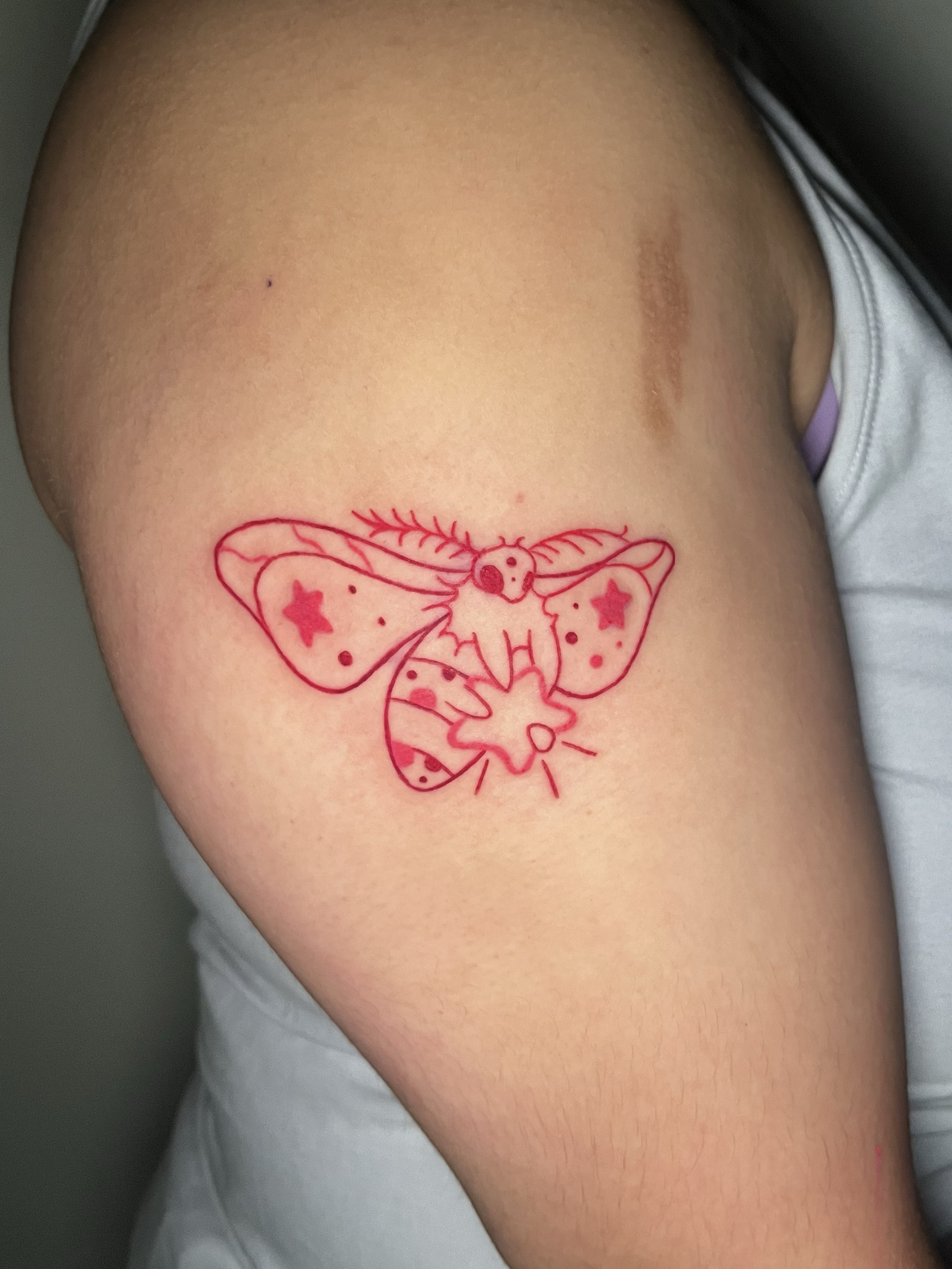 A close-up of a person's upper arm with a red outline of a butterfly tattoo, featuring stars and dots within its wings.
