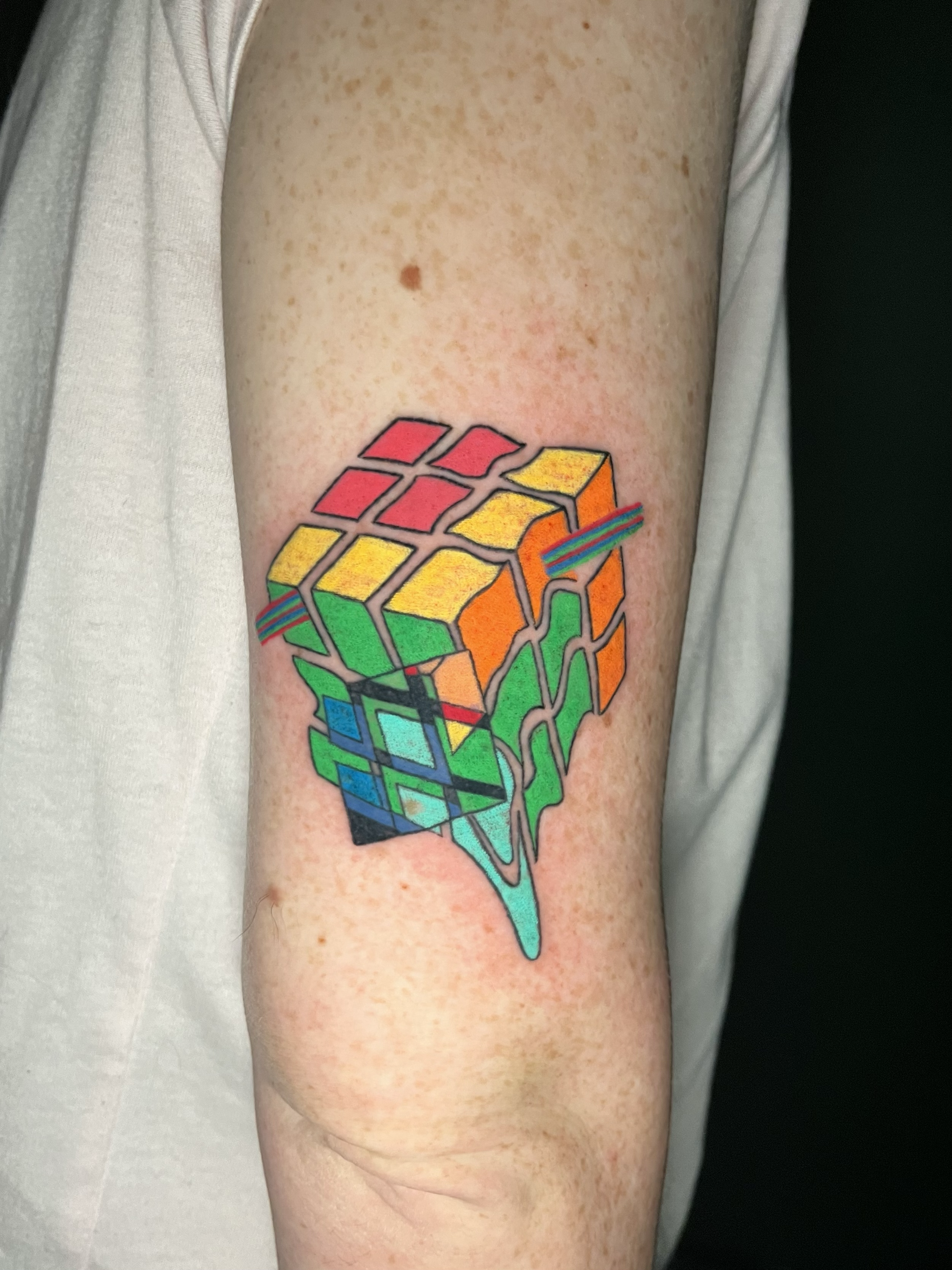 A tattoo of a colorful Rubik's Cube puzzle on a person's upper arm.