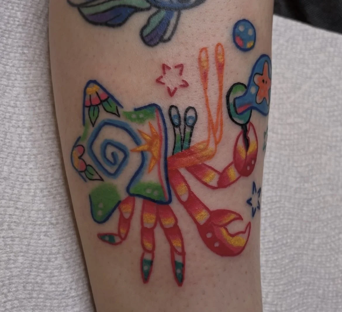 Colorful tattoo of a crab with decorative and patterned details on a person's arm.