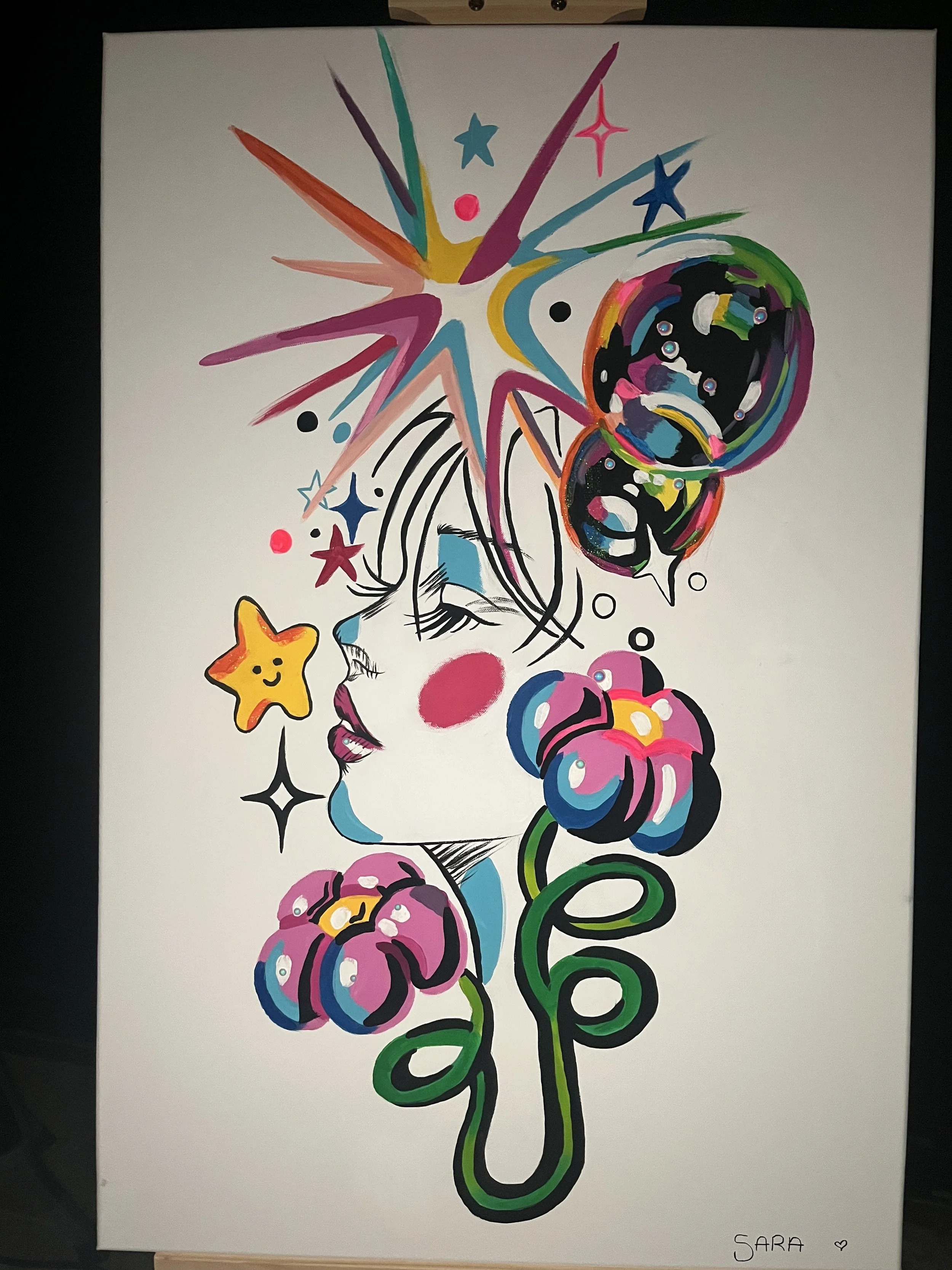 A colorful abstract painting with star, heart, and bubble shapes. It features a star, a smiley star, a face, and swirling lines in pink, purple, blue, green, yellow, black, and white. The bottom right corner is marked with the name "Sara" and a small heart.