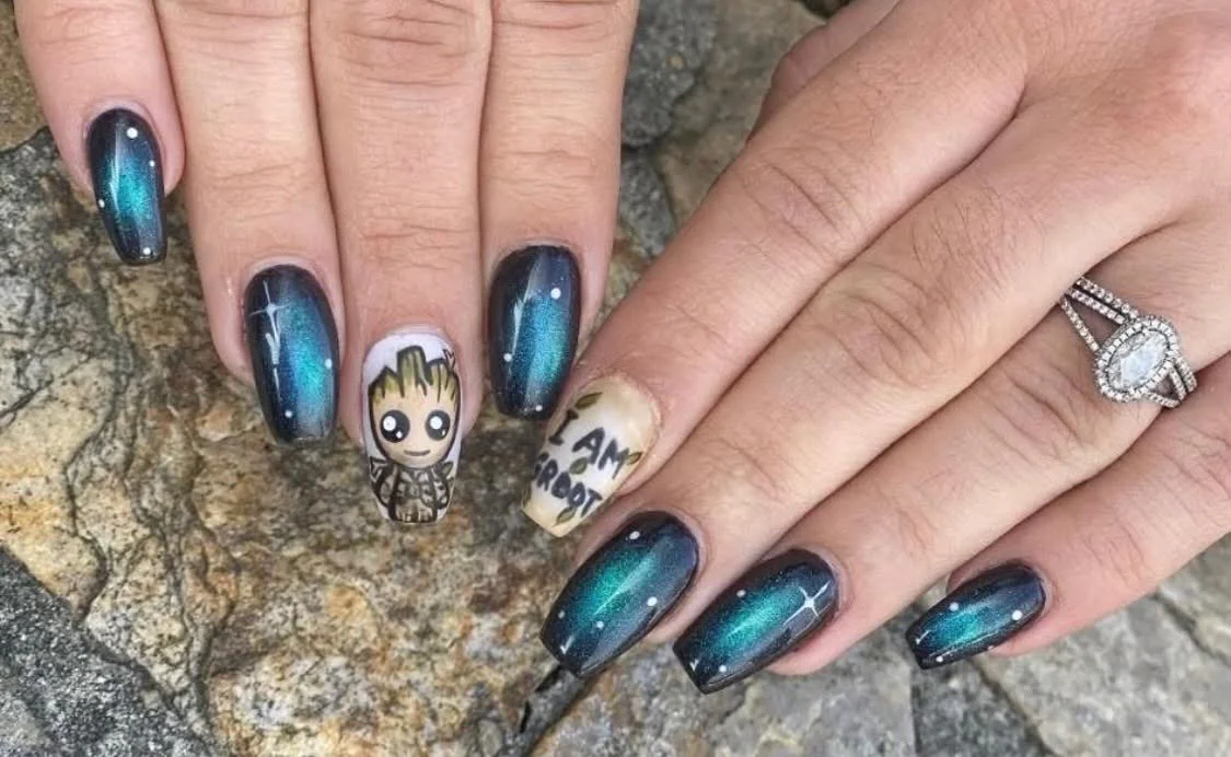 Manicured nails with galaxy-themed nail art, featuring a Groot cartoon on one nail and a message that reads "I AM GROOT" on another, with a stone ring on the right hand's ring finger.