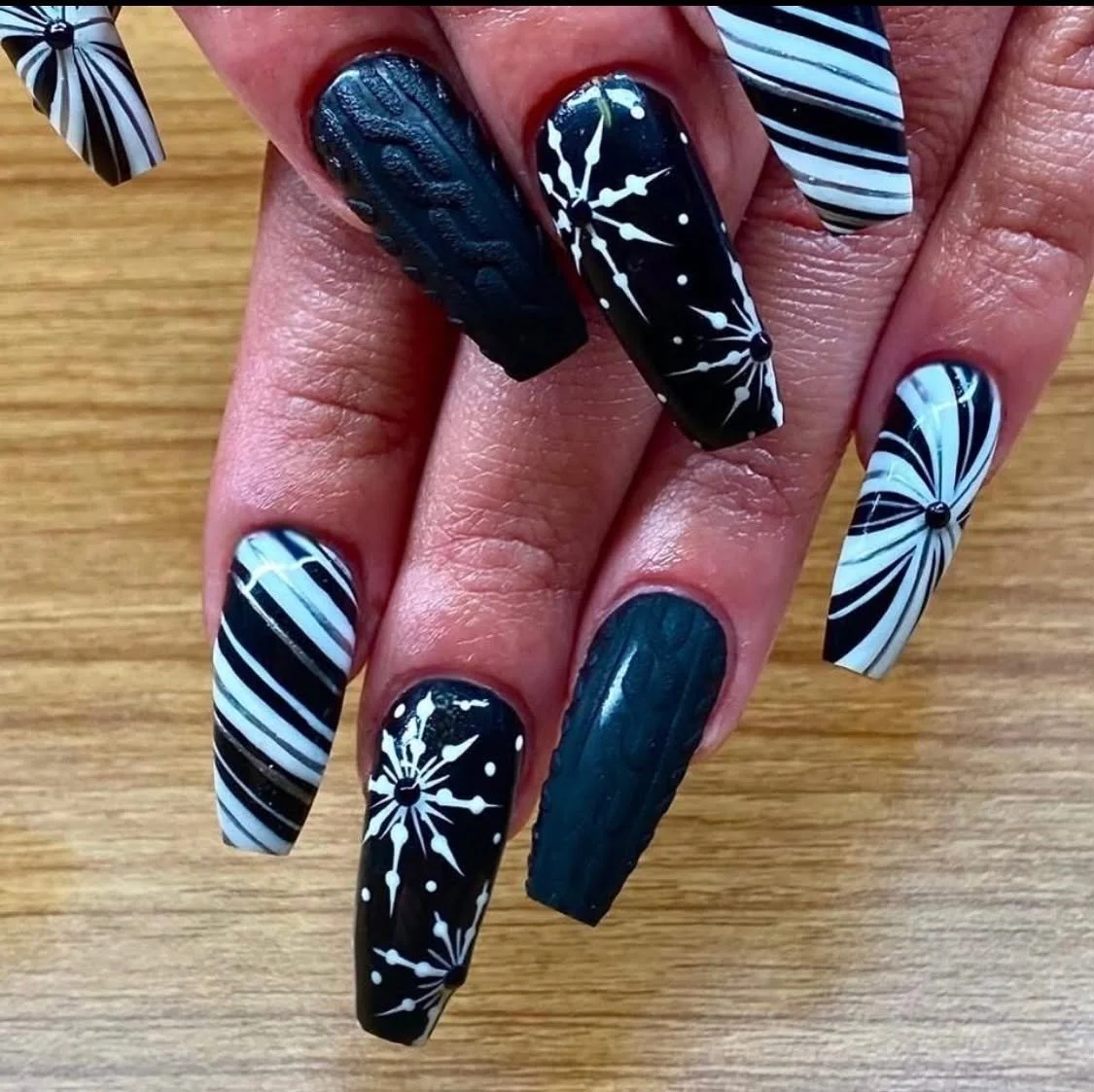 Close-up of decorated fingernails with black and white starburst and striped patterns on long nails.