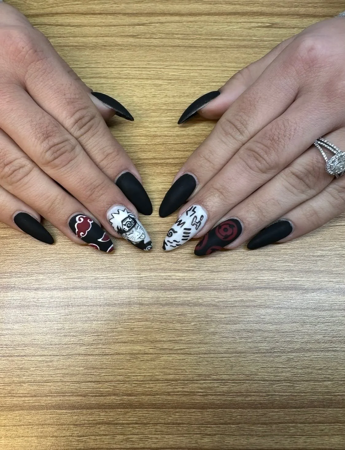 Close-up of hands with black matte and detailed anime-themed nail art on a wooden surface.