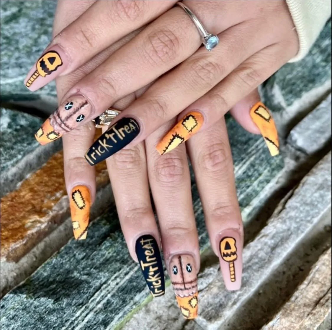 Nail art featuring Halloween-themed designs with orange, black, and cream colors, including pumpkins, candy, and the words 'Trick or Treat'.