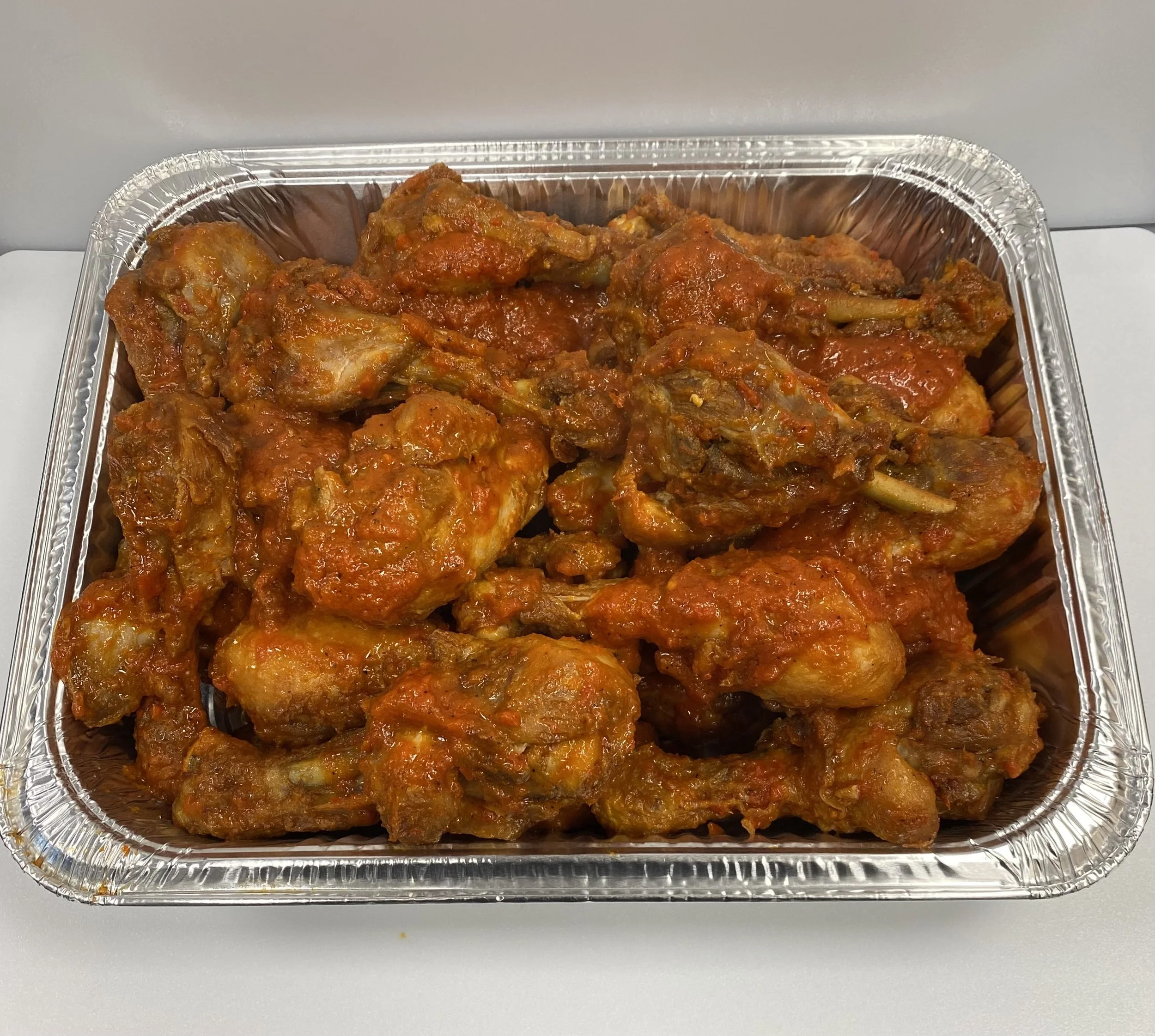 Aluminum tray filled with cooked chicken pieces in red sauce.