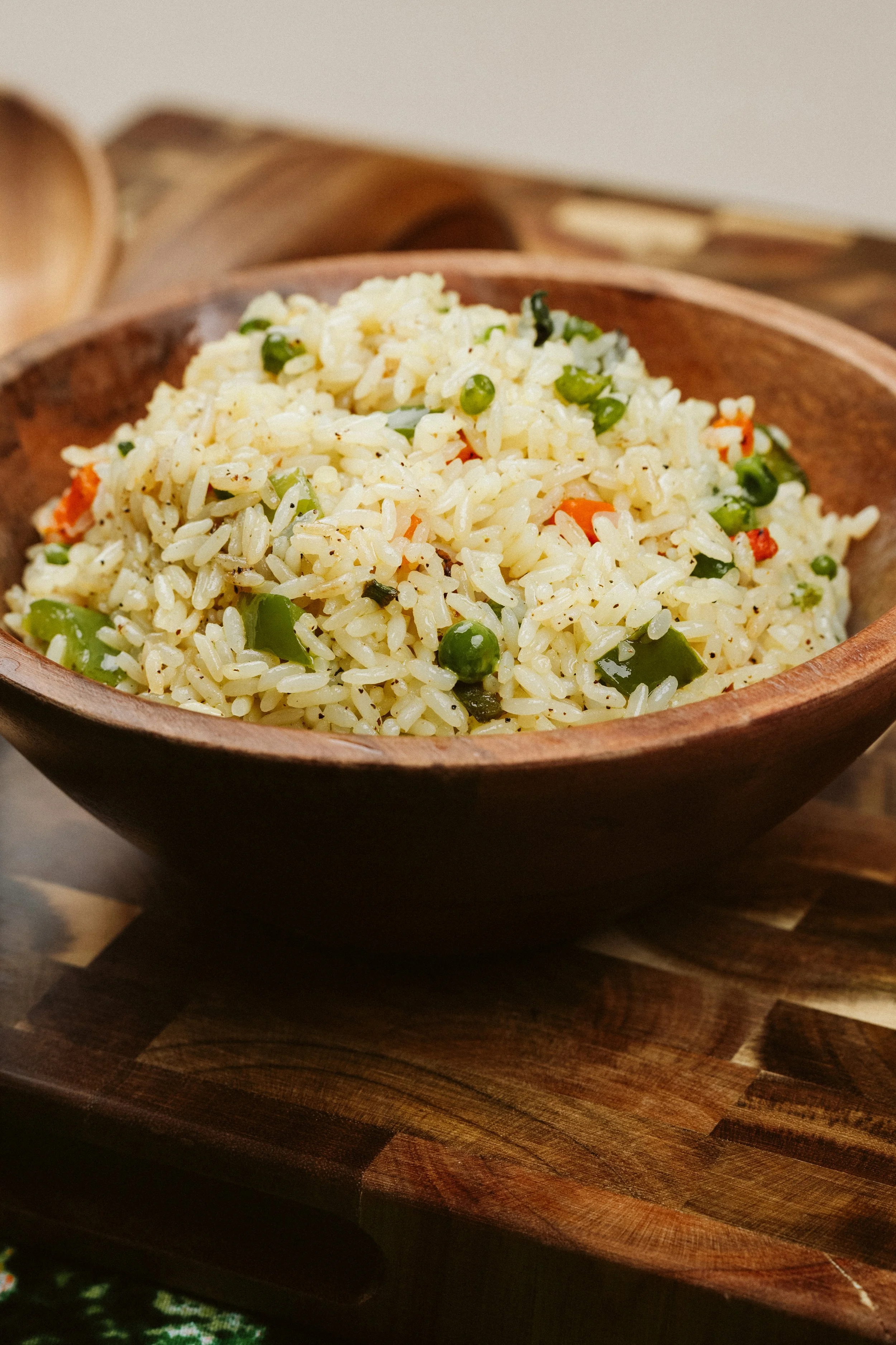 A bowl of cooked rice mixed with chopped green beans and small pieces of carrots on a wooden surface.
