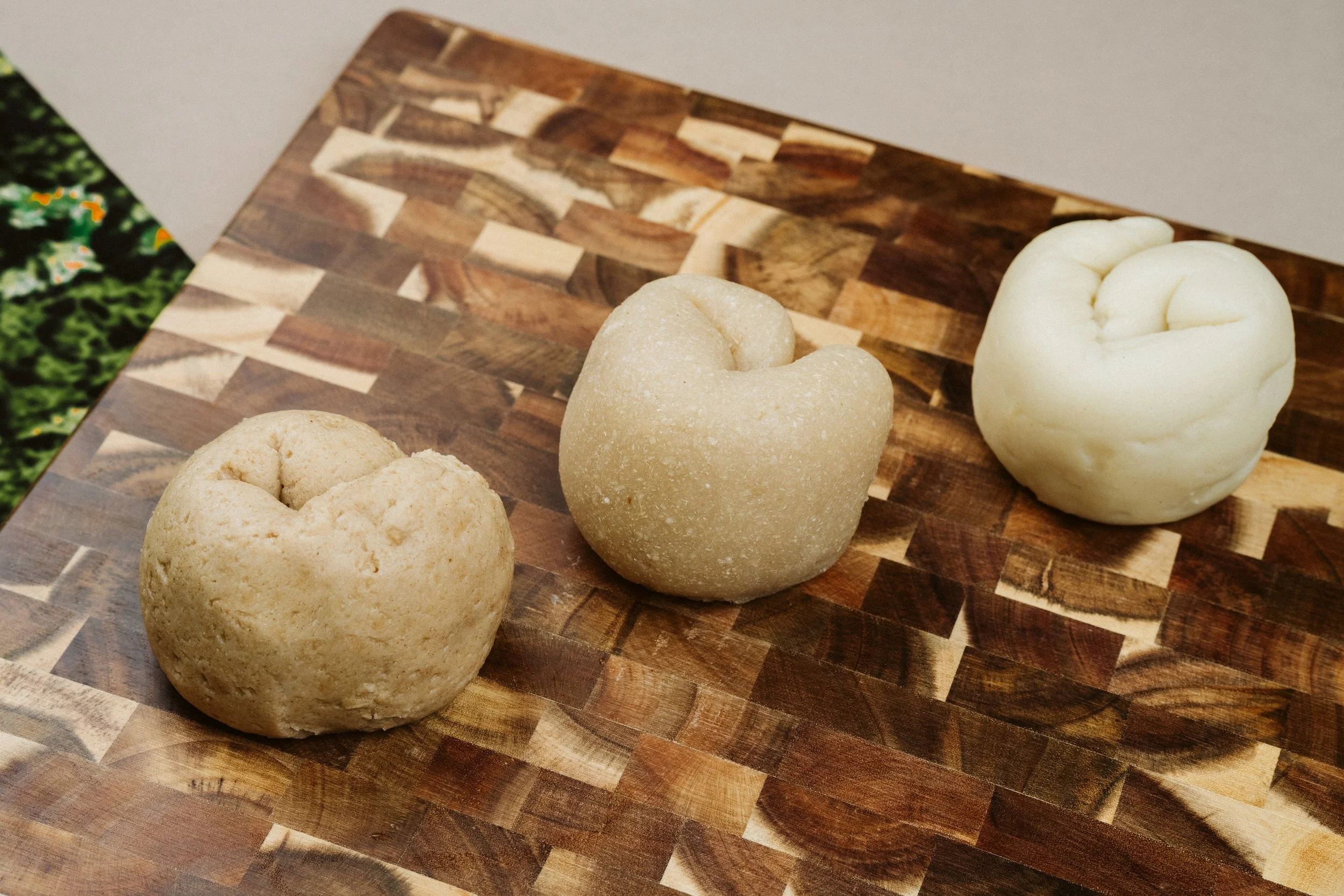 Three balls of cheese on a wooden cutting board.