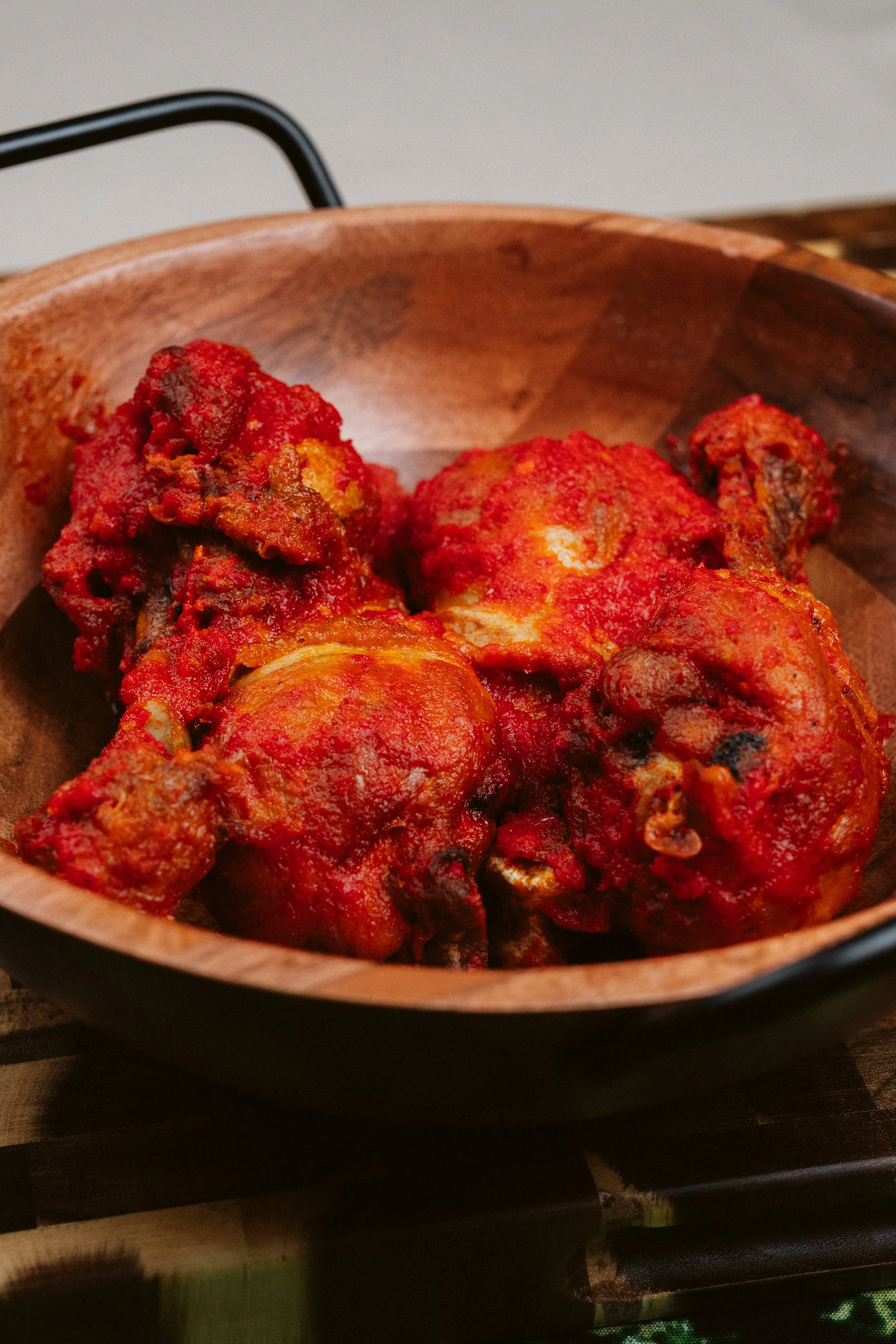 Close-up of cooked chicken pieces covered in red tomato sauce in a round wooden bowl.