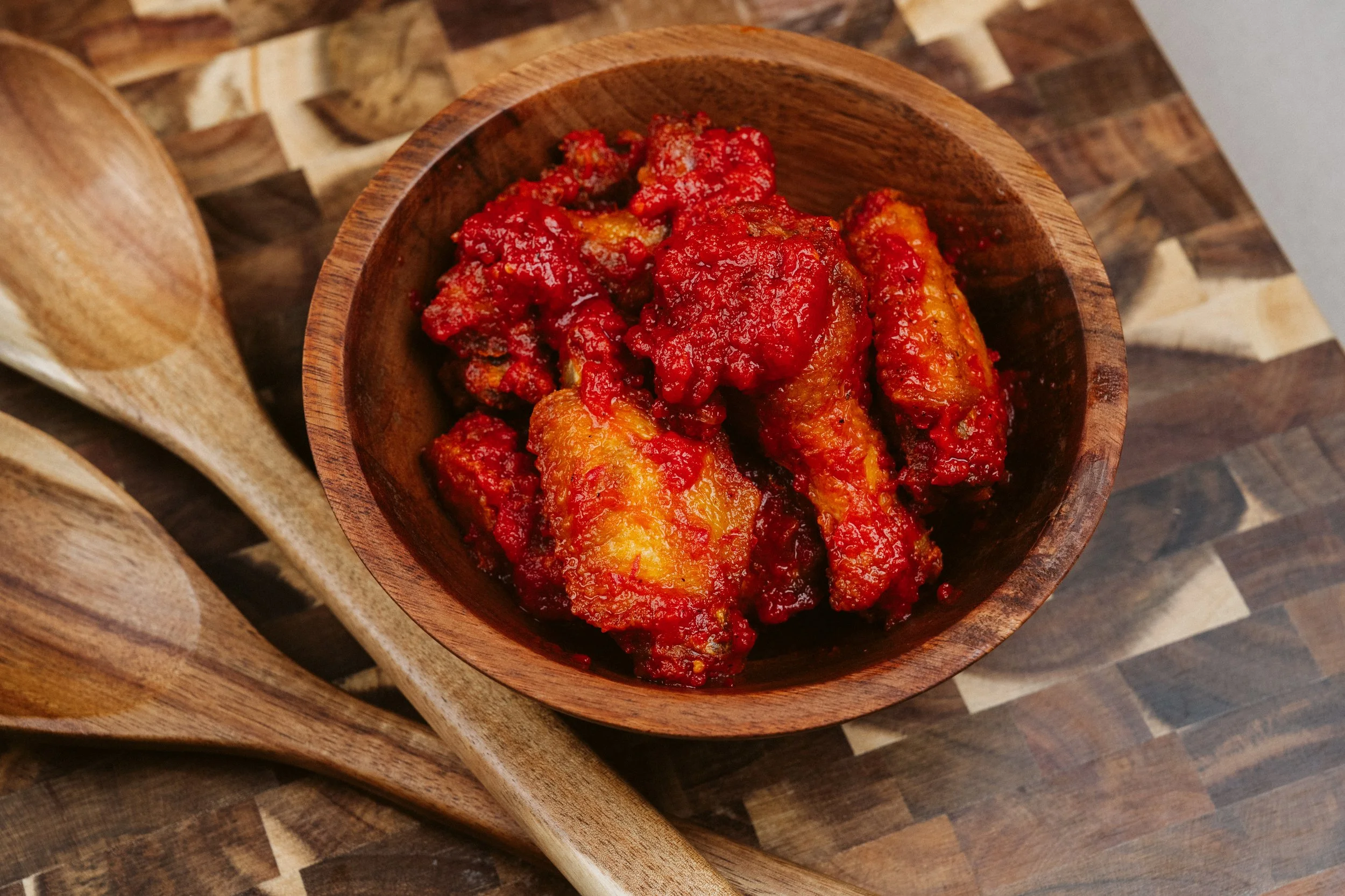 Wooden bowl filled with spicy buffalo chicken wings covered in red sauce, placed on a wooden table.