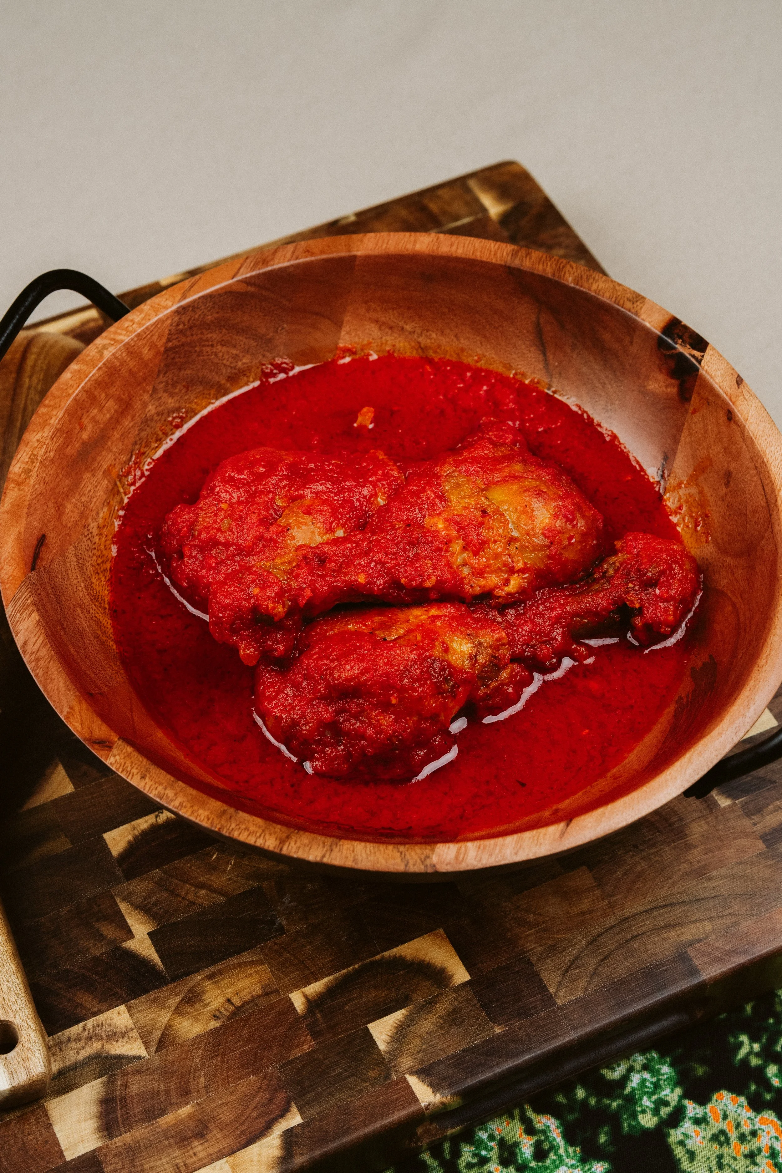 A wooden bowl filled with meatballs in marinara sauce on a wooden cutting board.
