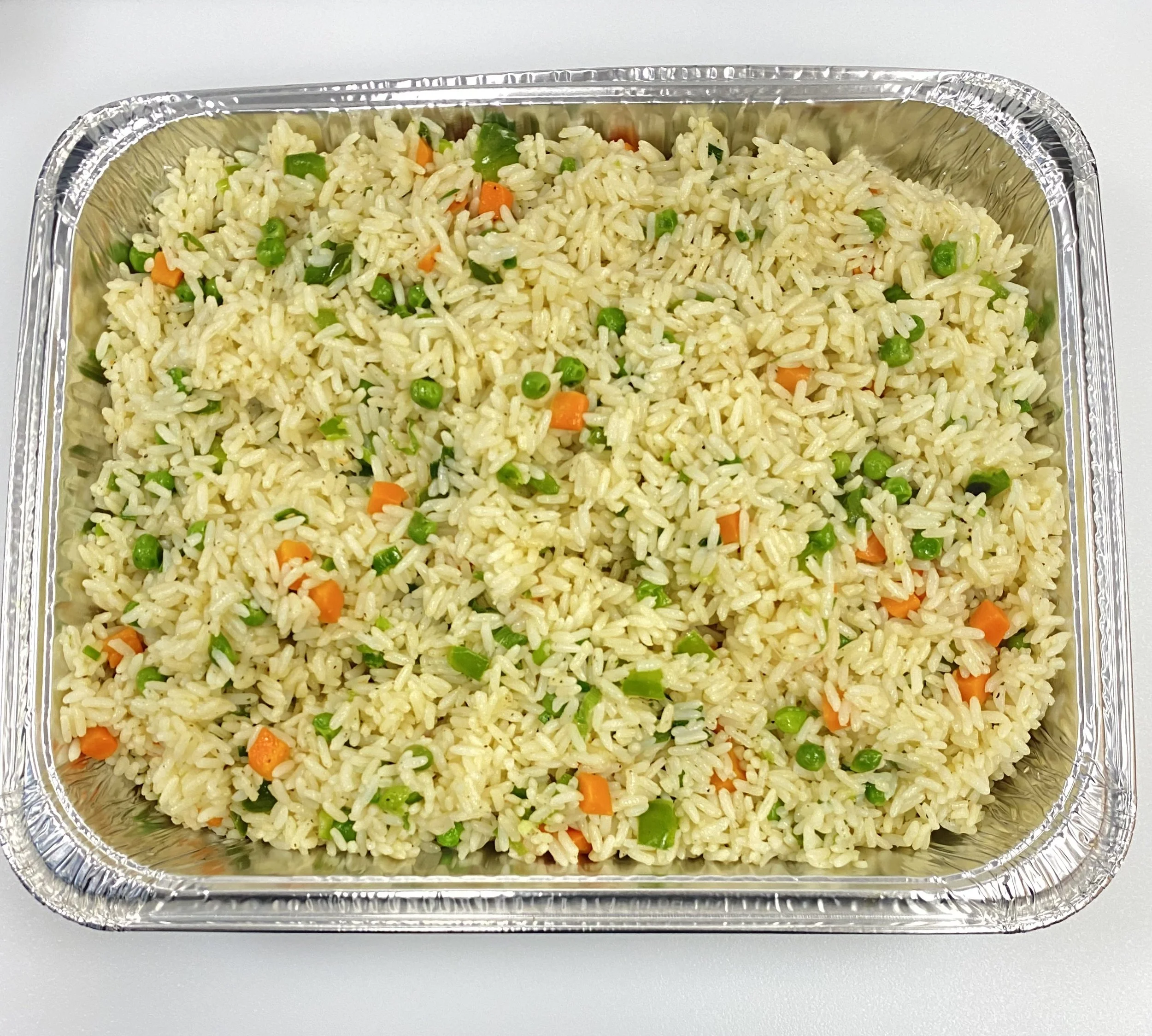 Aluminum tray filled with cooked fried rice with peas and small carrot pieces on a white surface.