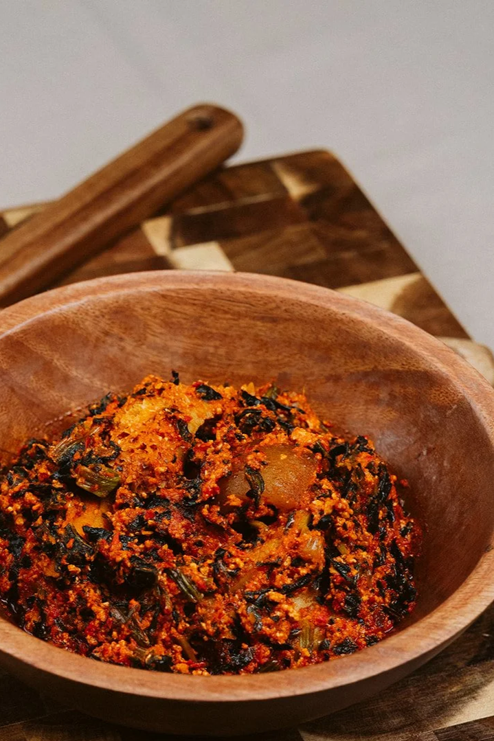 A wooden bowl filled with a spicy, textured mixture that appears to be a vegetable or meat dish, possibly seasoned and cooked with spices and herbs.
