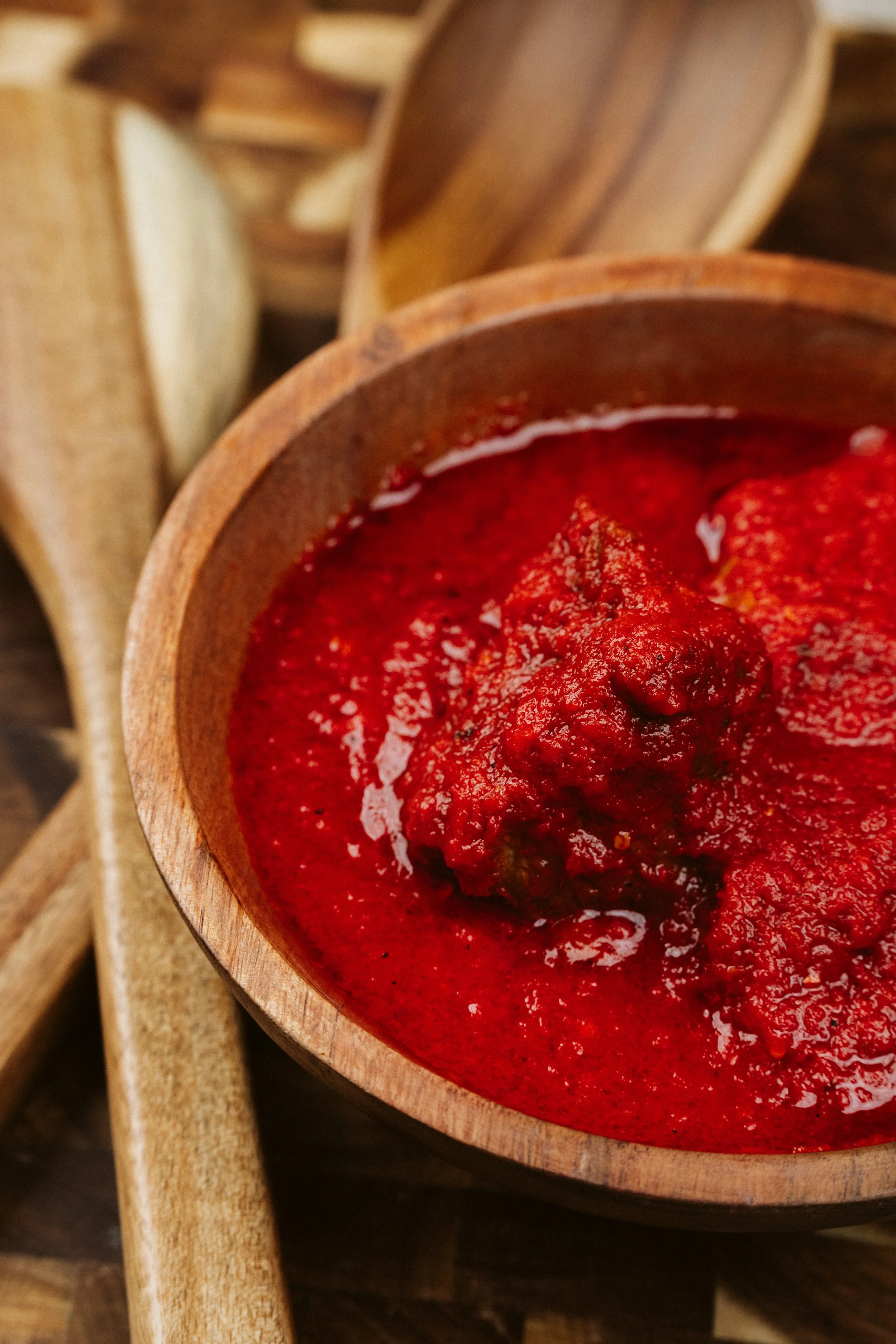 Close-up of a wooden bowl filled with red tomato sauce, placed on a wooden surface.