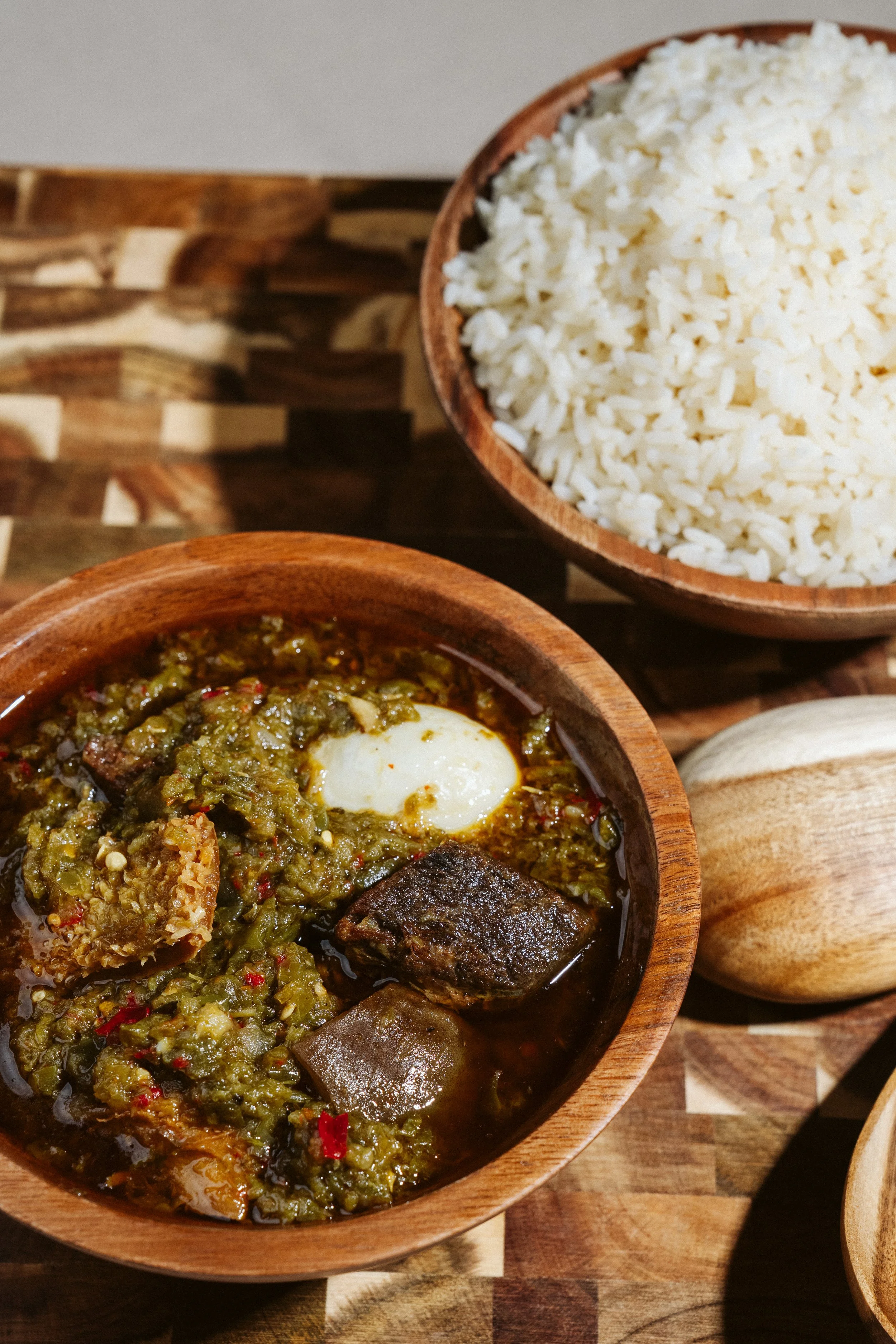 A bowl of chili with a poached egg and meat, alongside a bowl of cooked white rice on a wooden surface.