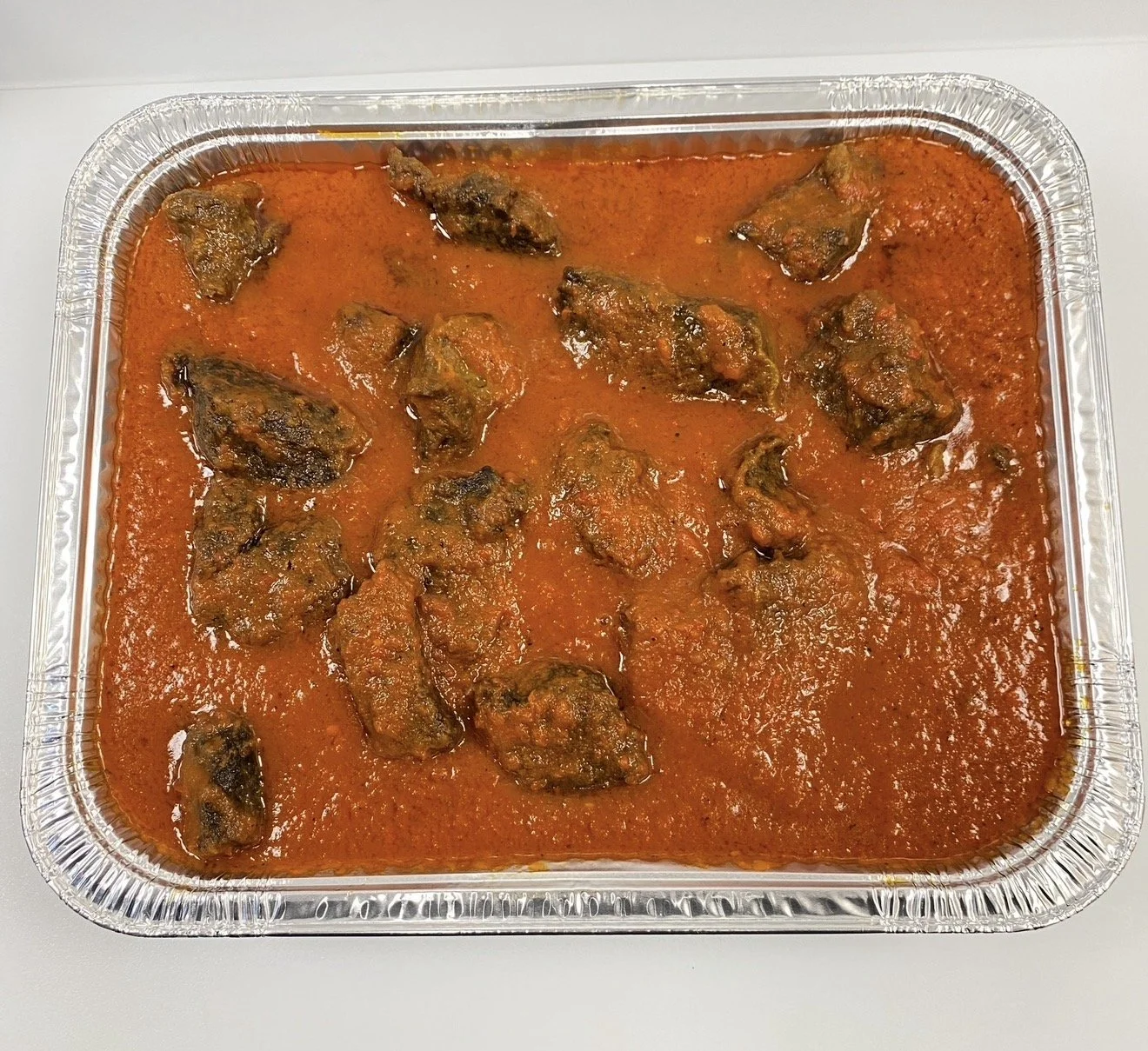Beef stew with chunks of beef in a red sauce in a silver food container.