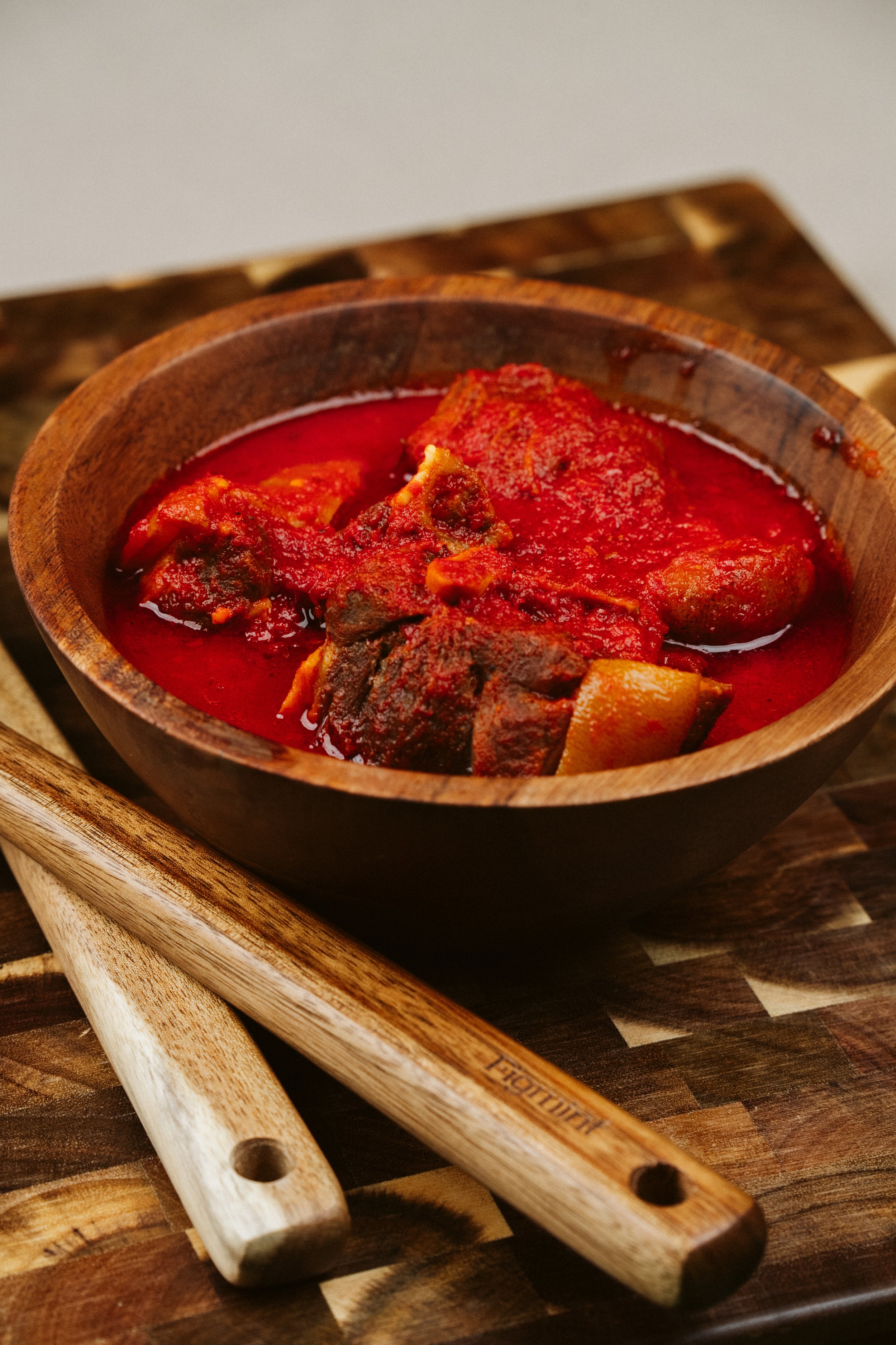 A bowl of spicy red stew with chunks of meat, garnished with sauce, placed on a round wooden tray.
