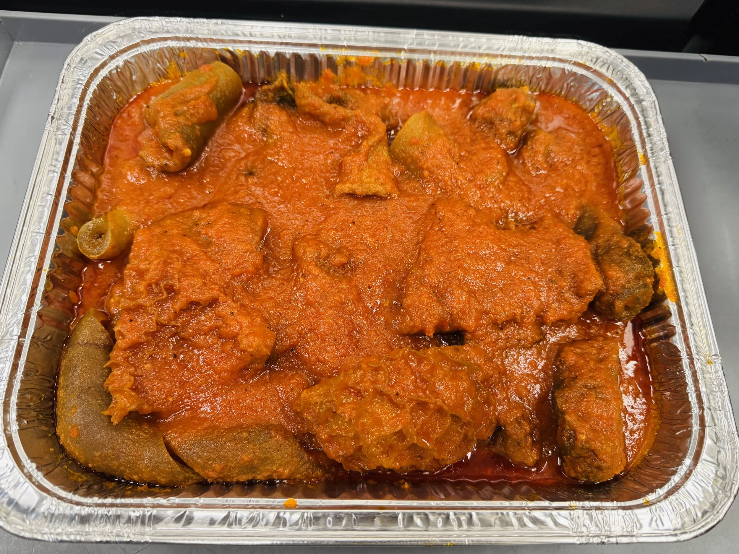 Aluminium tray containing meat curry with rice and possibly vegetables in a red tomato-based sauce.