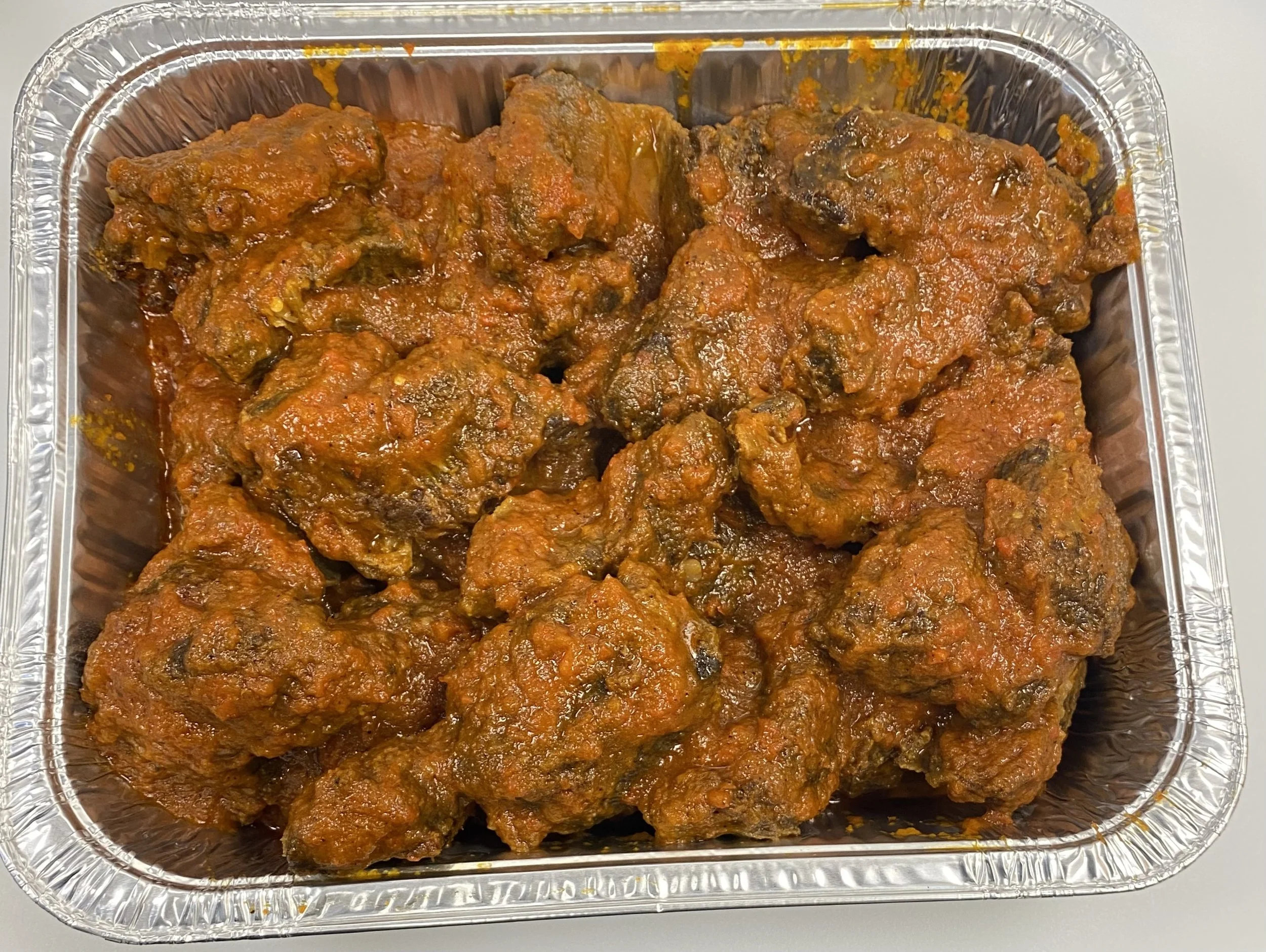 Aluminum container filled with cooked spicy meat chunks in reddish sauce.