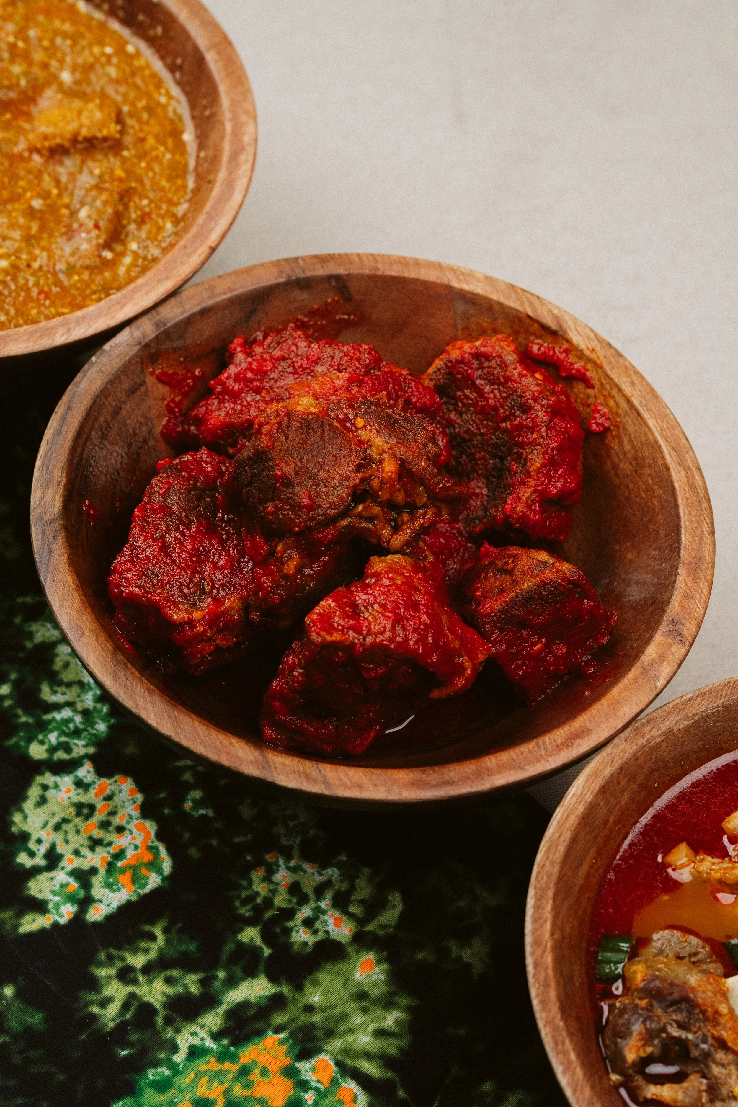 Close-up of small wooden bowls containing different spicy Indian dishes on a colorful traditional cloth.
