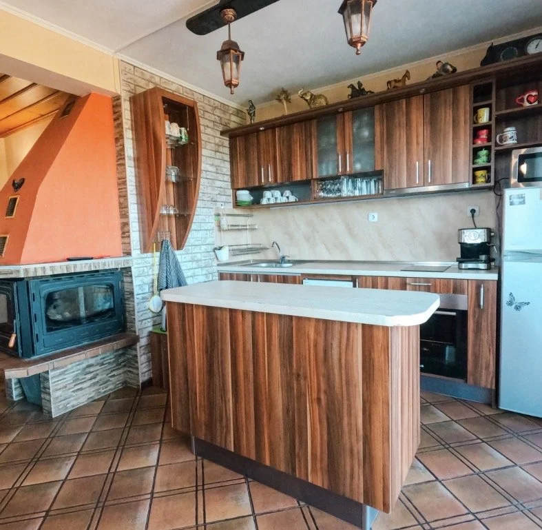 Kitchen with wooden cabinets, a brick wall, a white countertop island, and a tiled floor. Includes a microwave oven, a refrigerator with a butterfly sticker, and decorative animal figurines on the upper cabinets.