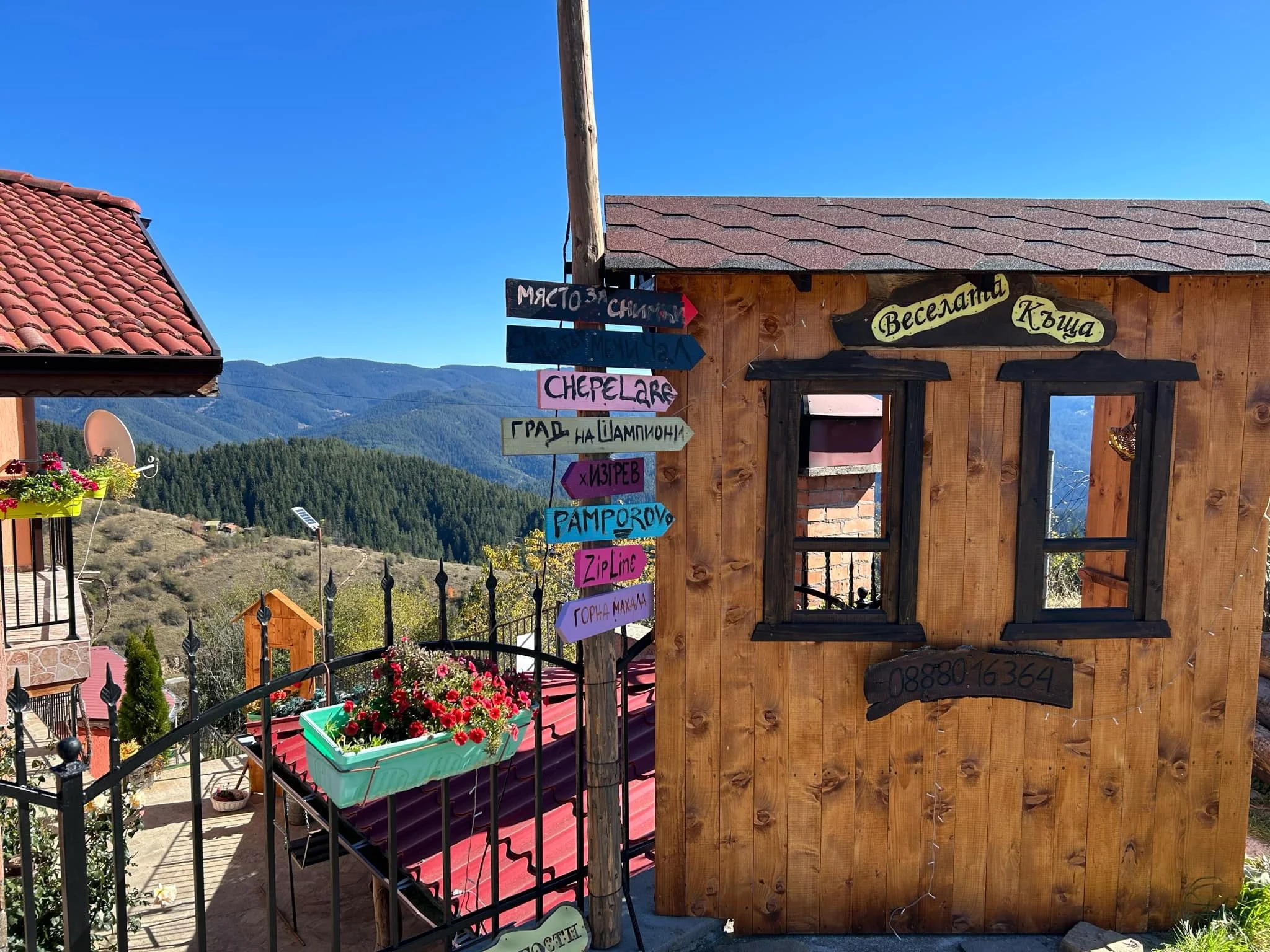 View of a rustic wooden building with colorful street signs in front, set against a backdrop of mountains and a bright blue sky.