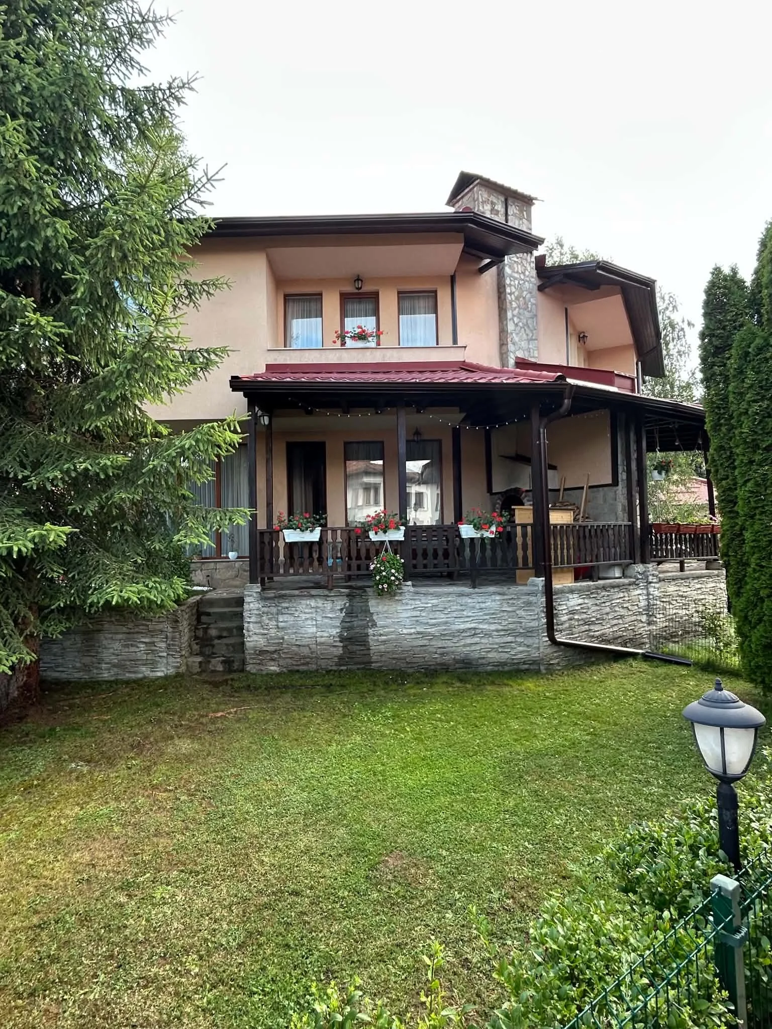 Front yard with a grassy lawn, green shrubs, a lamppost, and a two-story house with a covered porch, balcony, and windows with flower boxes.